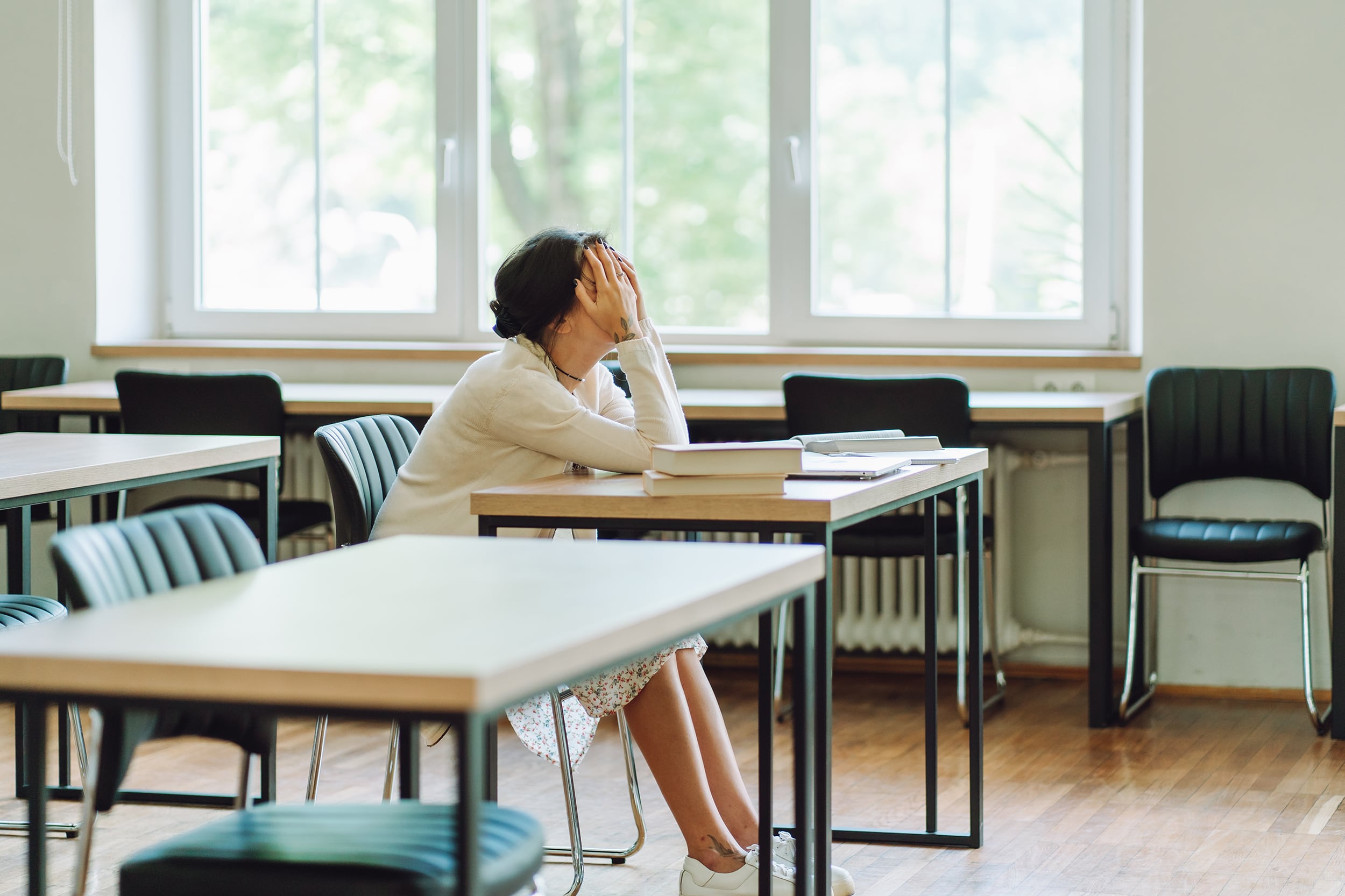 A photograph of a stressed out teacher sitting with her head in her hands while sitting at a desk.