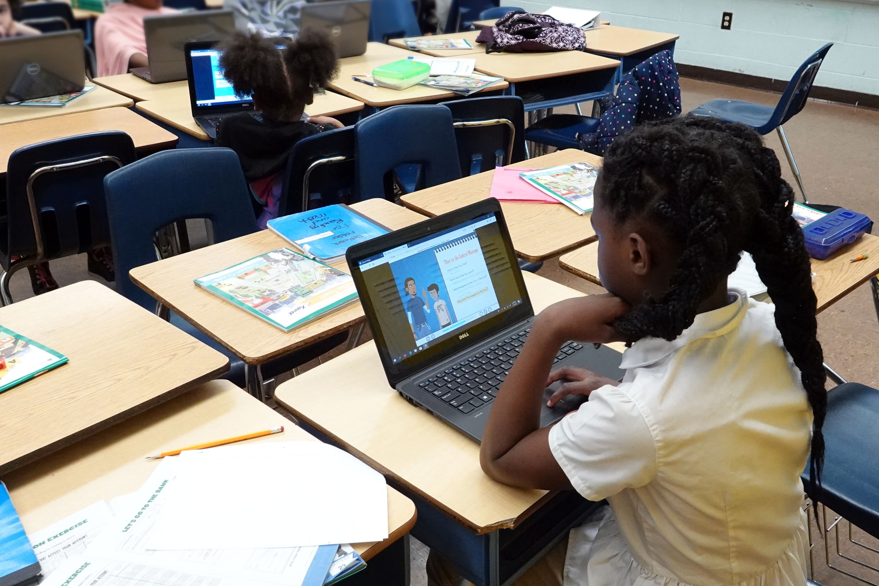 A photograph of a young Black student working at her desk on a computer in a classroom.