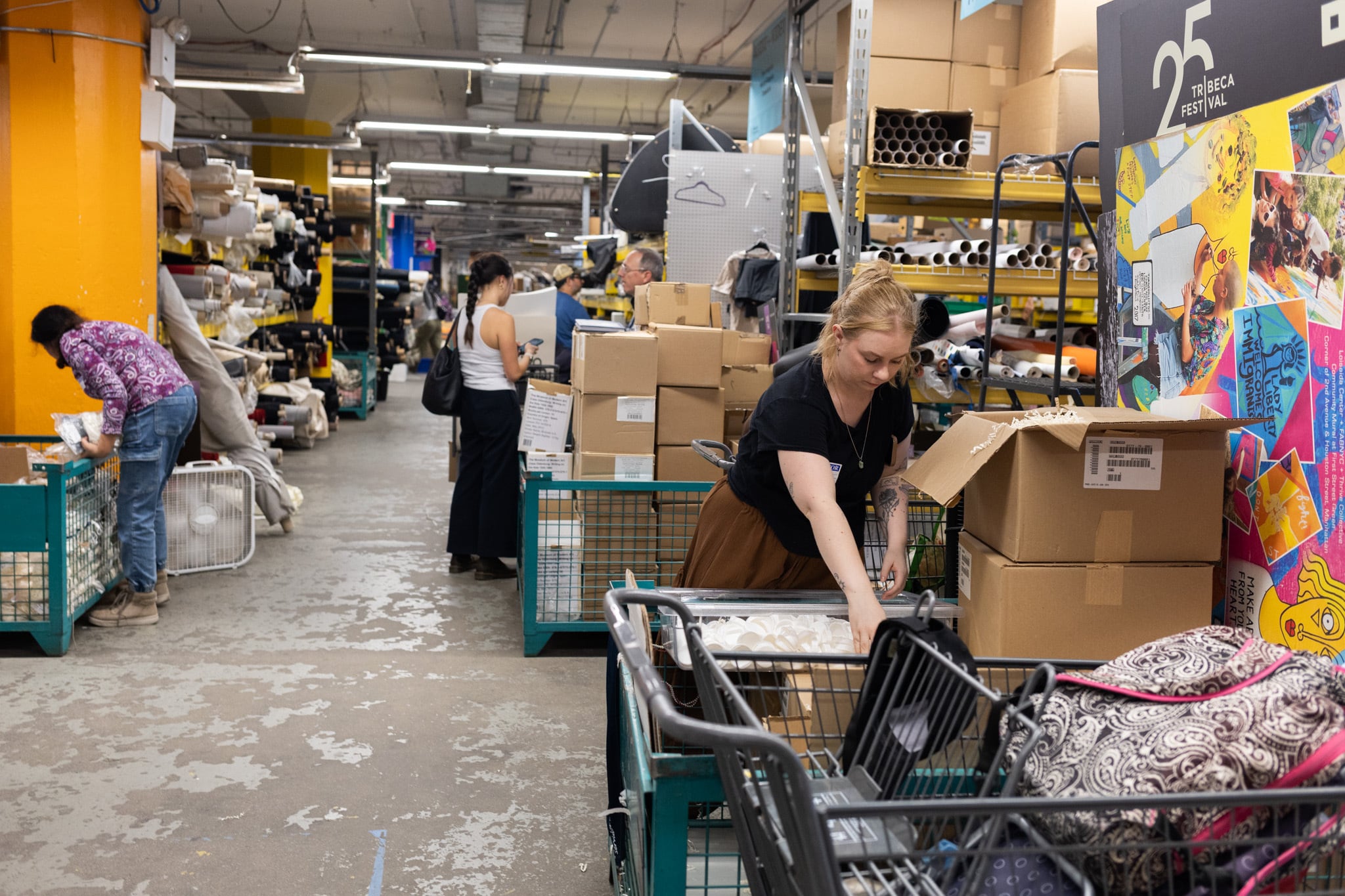 A woman works in the foreground of a large warehouse with boxes and people in the background.