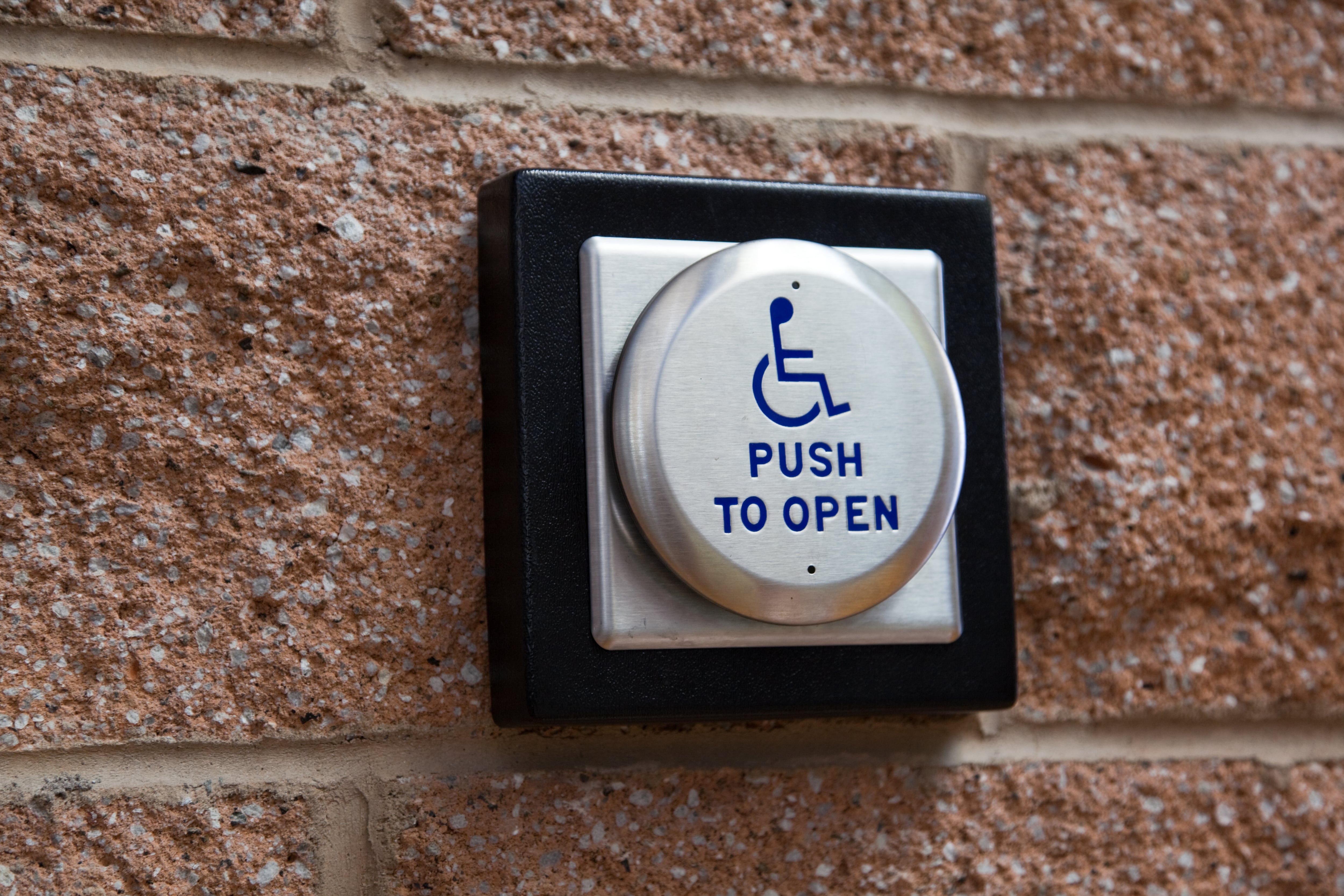 A button on a wall with a wheelchair icon. It says, "Push to open."
