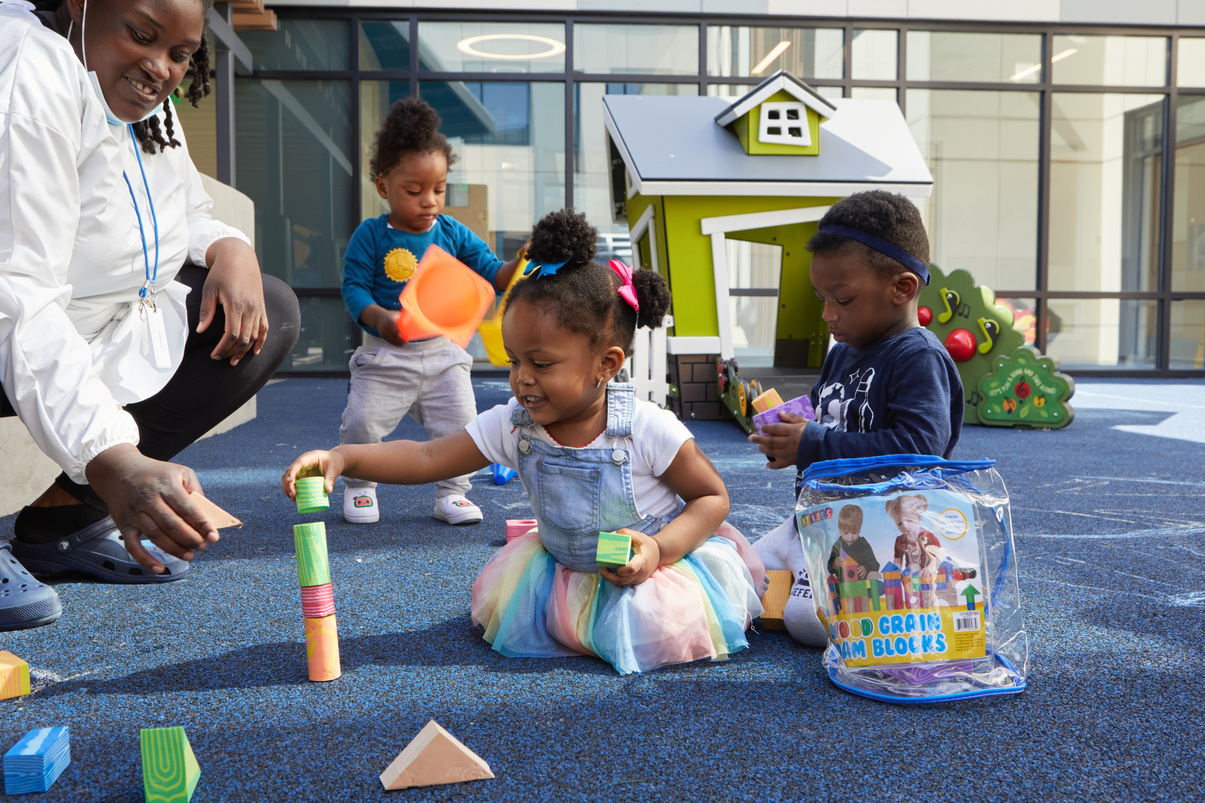 Three children and their teacher play with toys on the ground.