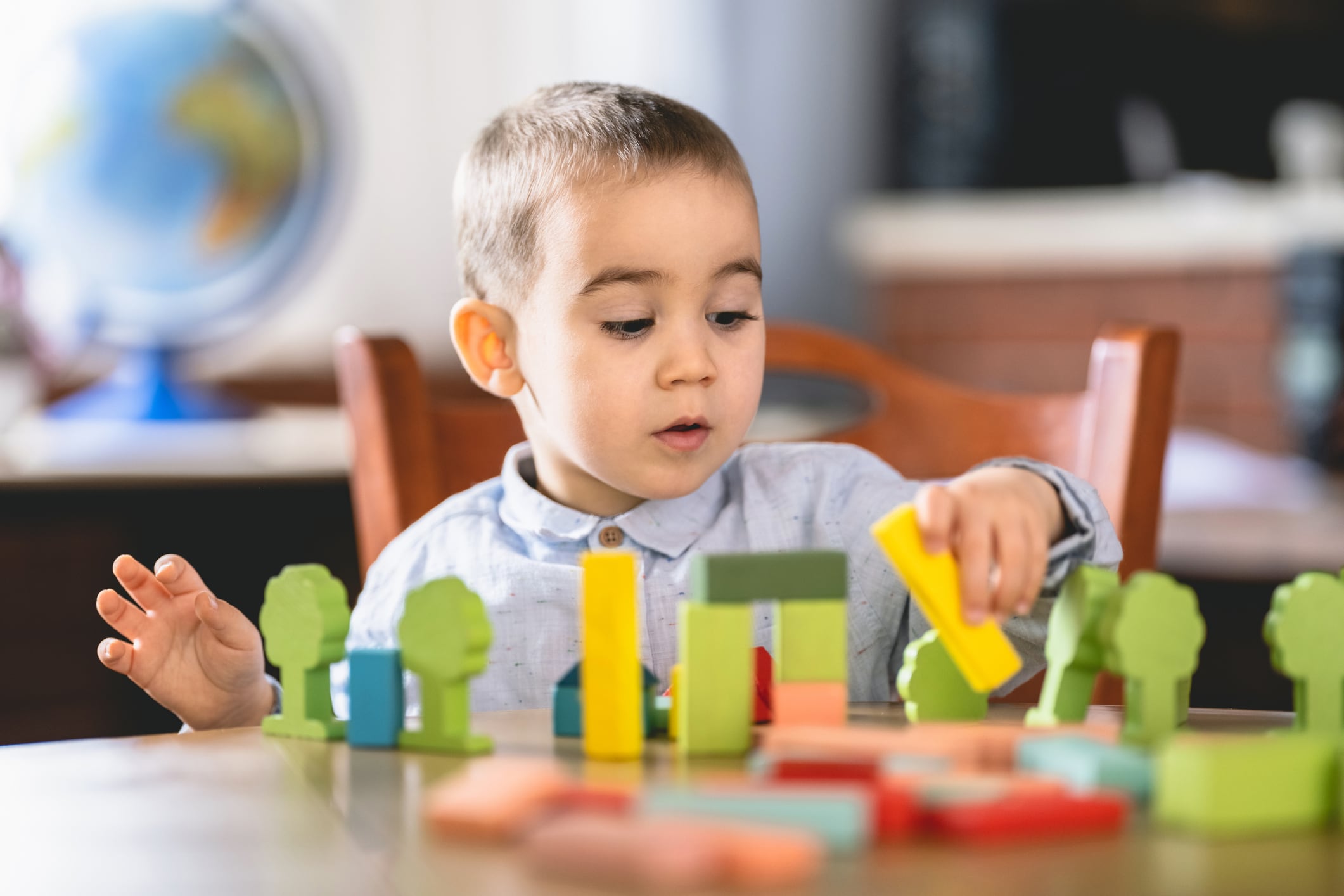 A little boy plays with multicolored blocks at a wooden desk.