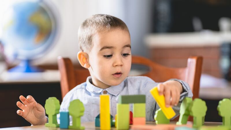 A little boy plays with multicolored blocks at a wooden desk.