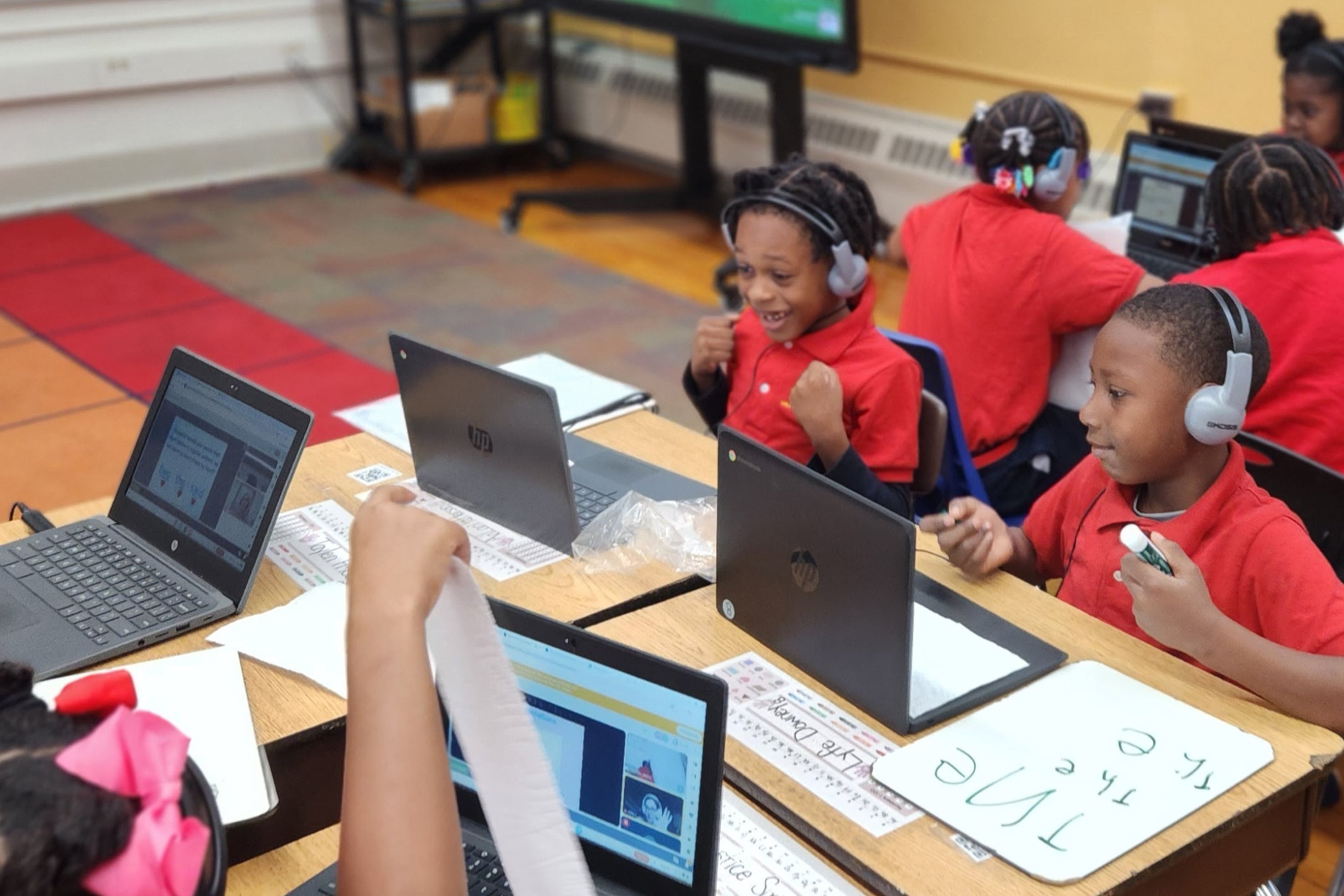 Students in red shirts sit at laptops in a classroom.
