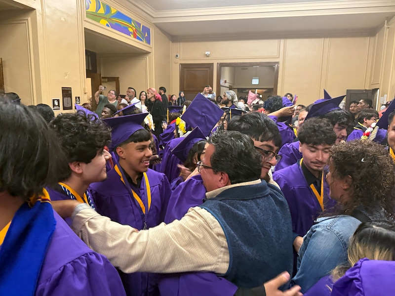 A photograph of a teacher greeting a student after graduation in a large crowd of people.