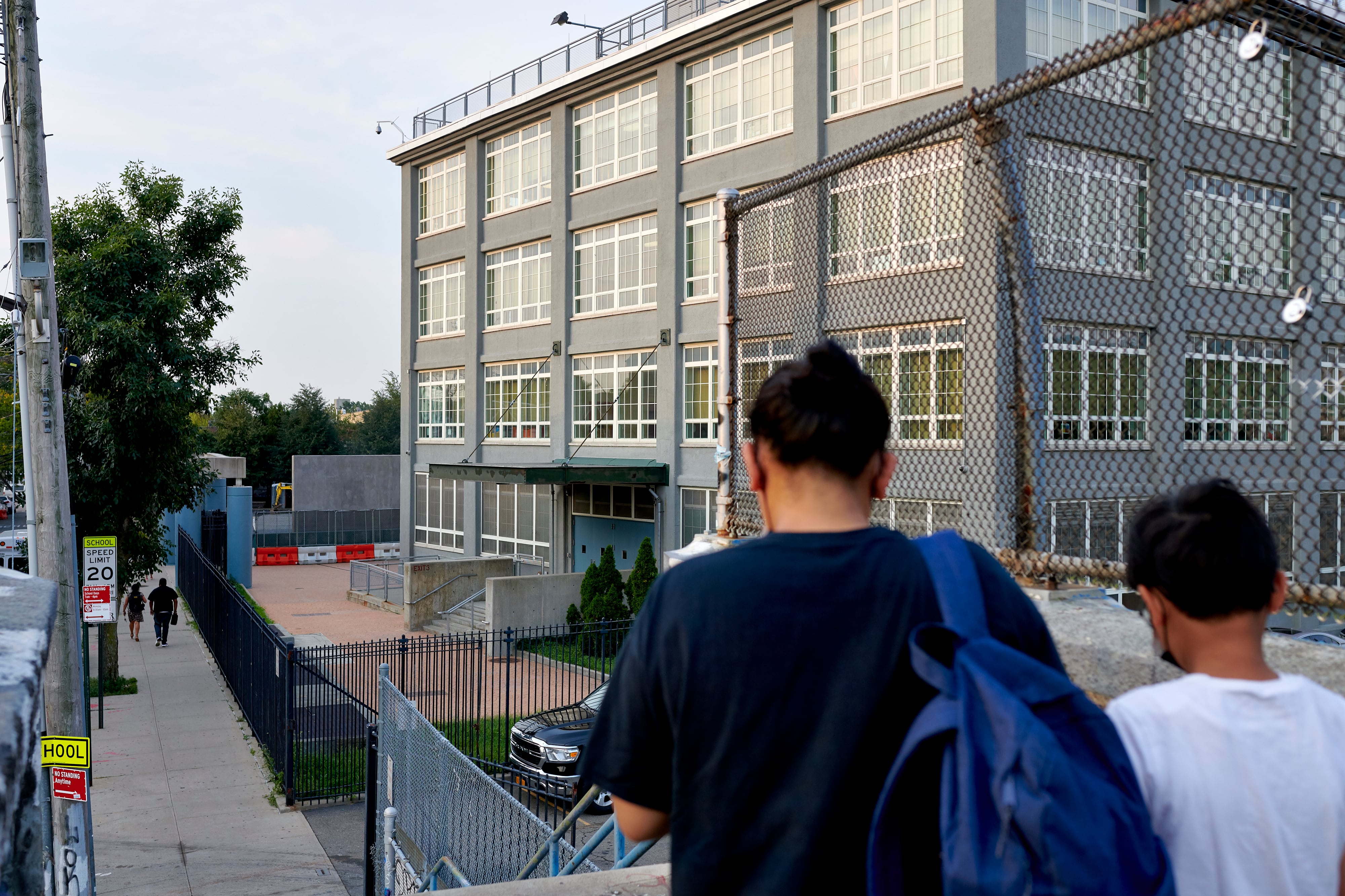 Two students walk down a set of stairs outside in front of a large school building.