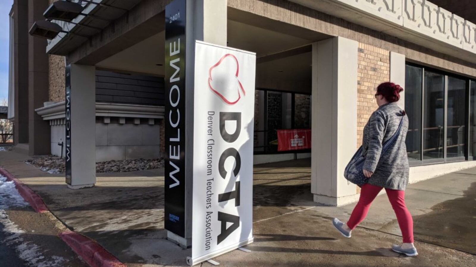 A woman wearing a coat walks into a building. The building has a banner on it that says “DCTA,” which stands for Denver Classroom Teachers Association.