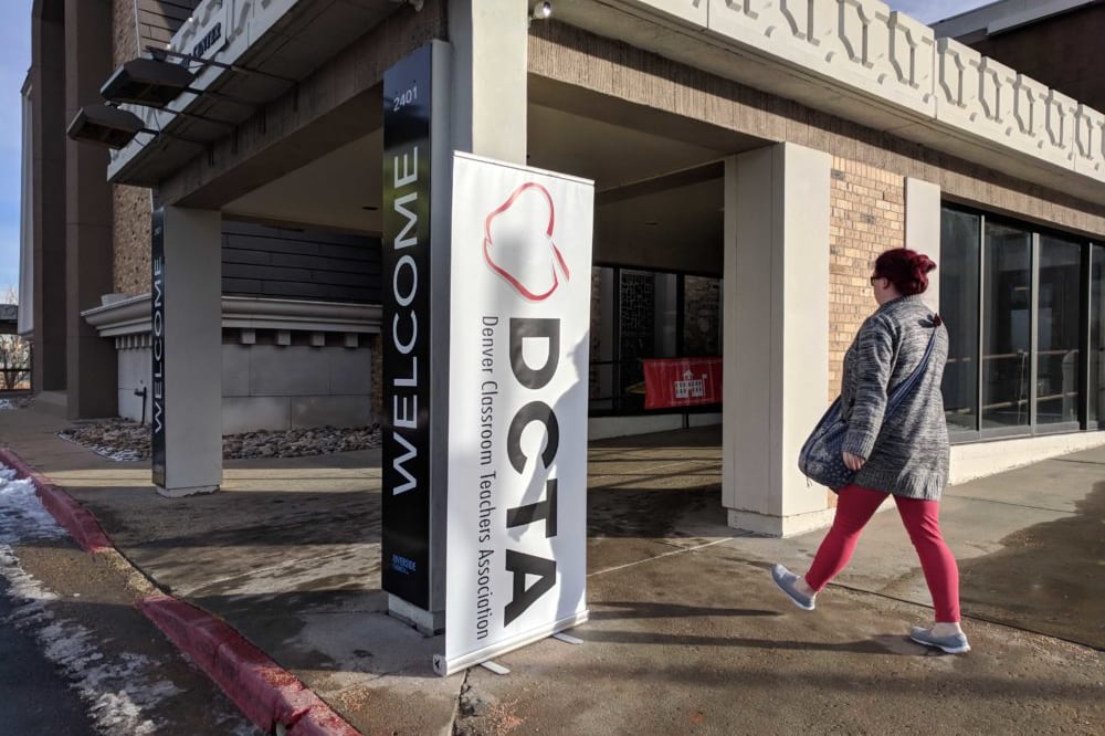A woman wearing a coat walks into a building. The building has a banner on it that says “DCTA,” which stands for Denver Classroom Teachers Association.