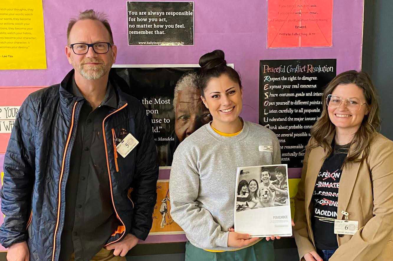 Three people stand next to each other while the person in the center holds a piece of paper. They smile and look at the camera for a portrait.