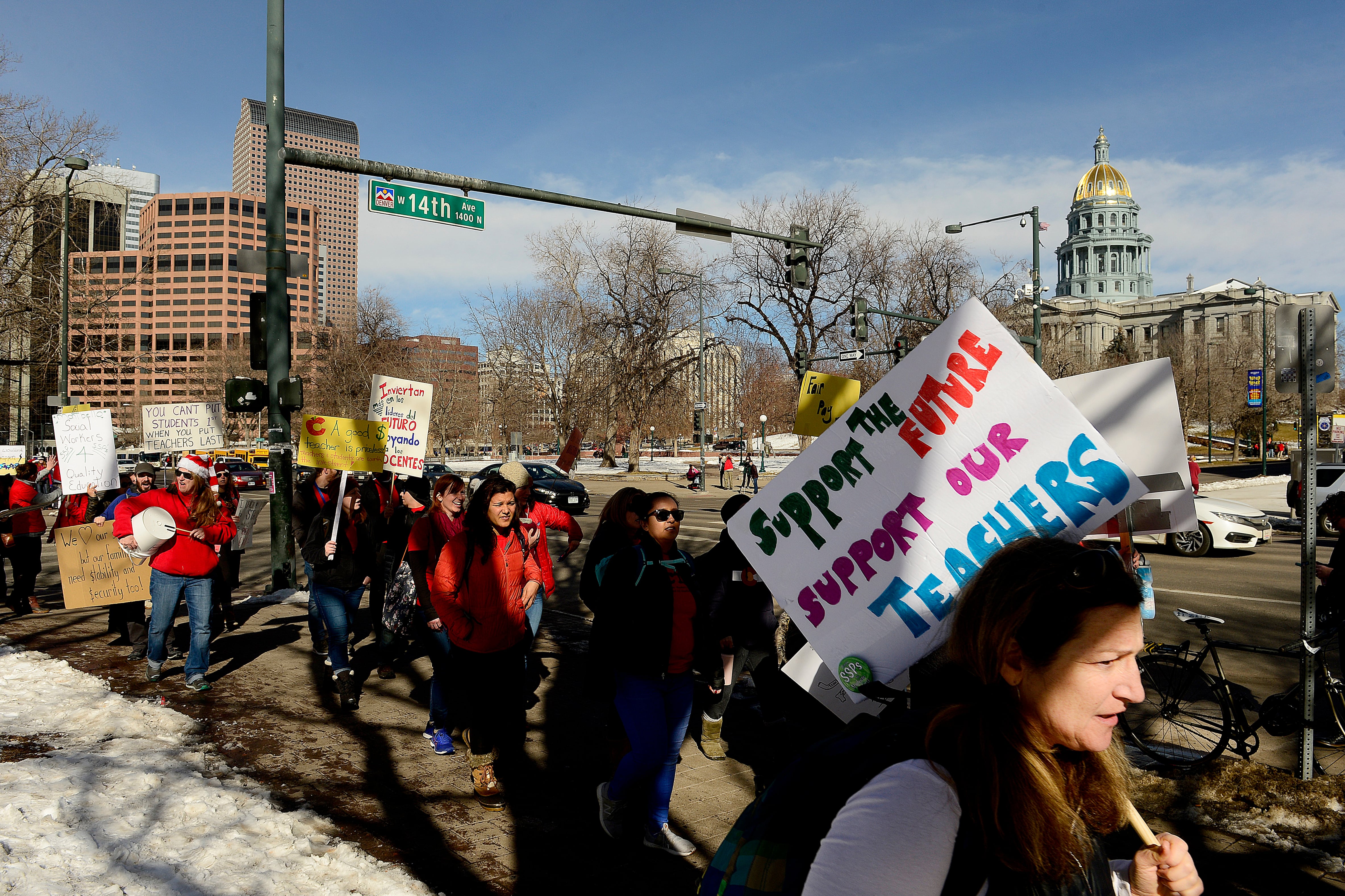 A group of teachers march outside the Colorado state Capitol building. Some are holding signs.
