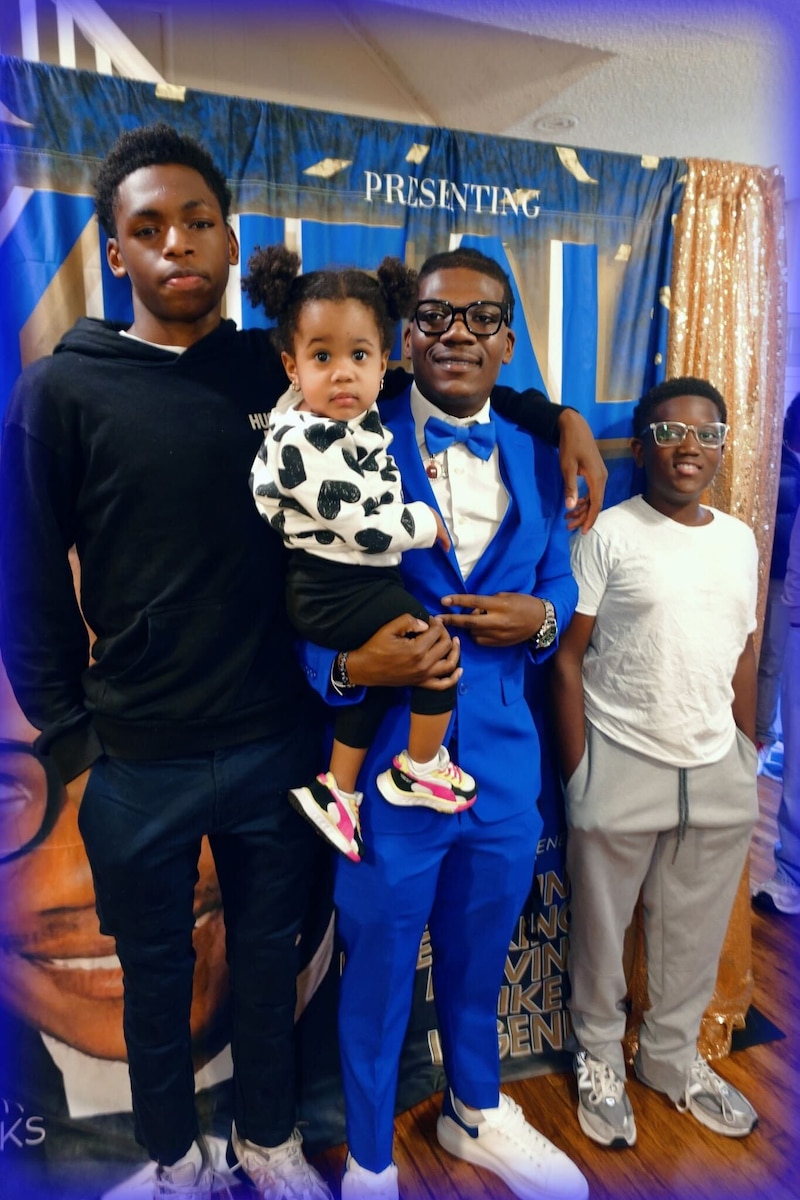 Four children of different ages pose for a photograph together in front of a banner.
