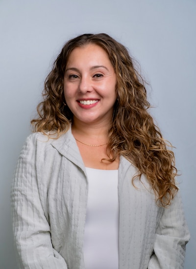 Headshot of a woman with long light brown hair. She is wearing a white shirt and a gray blazer.