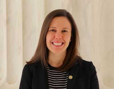 A woman in a black and white blouse and medium length brown hair poses for a portrait in front of a white background.