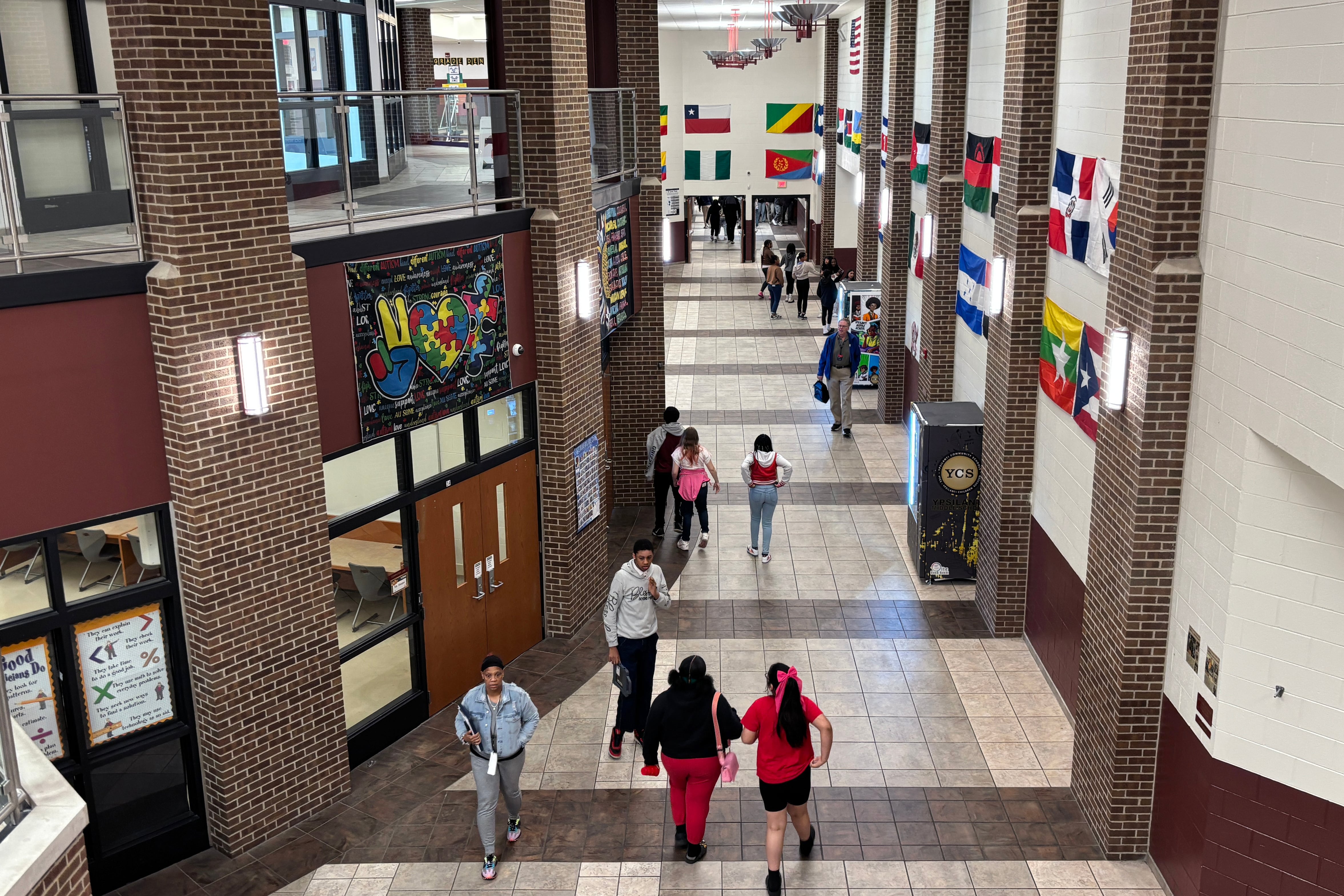 Middle school students walk down a large entry way with country flags on the walls.