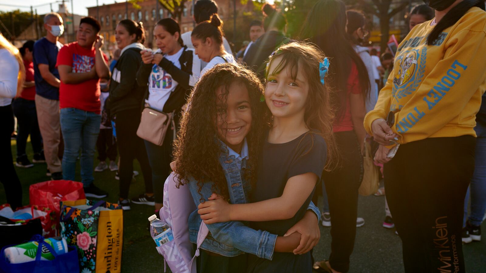 Two young girls hug each other for a portrait as parents and other children stand behind them.