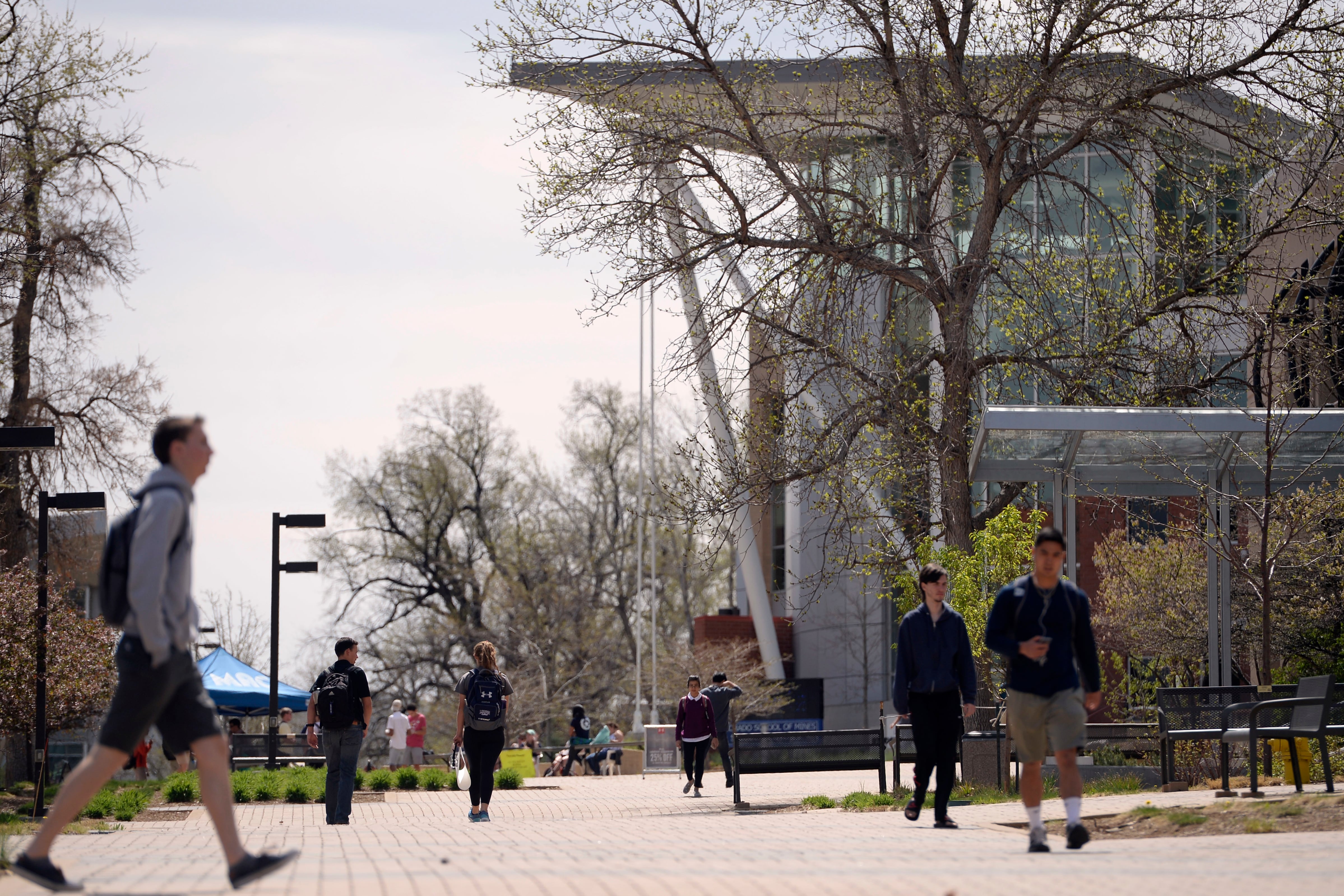 Students walk through a Colorado college campus, a large building with a flat roof looming in the background down the walkway.