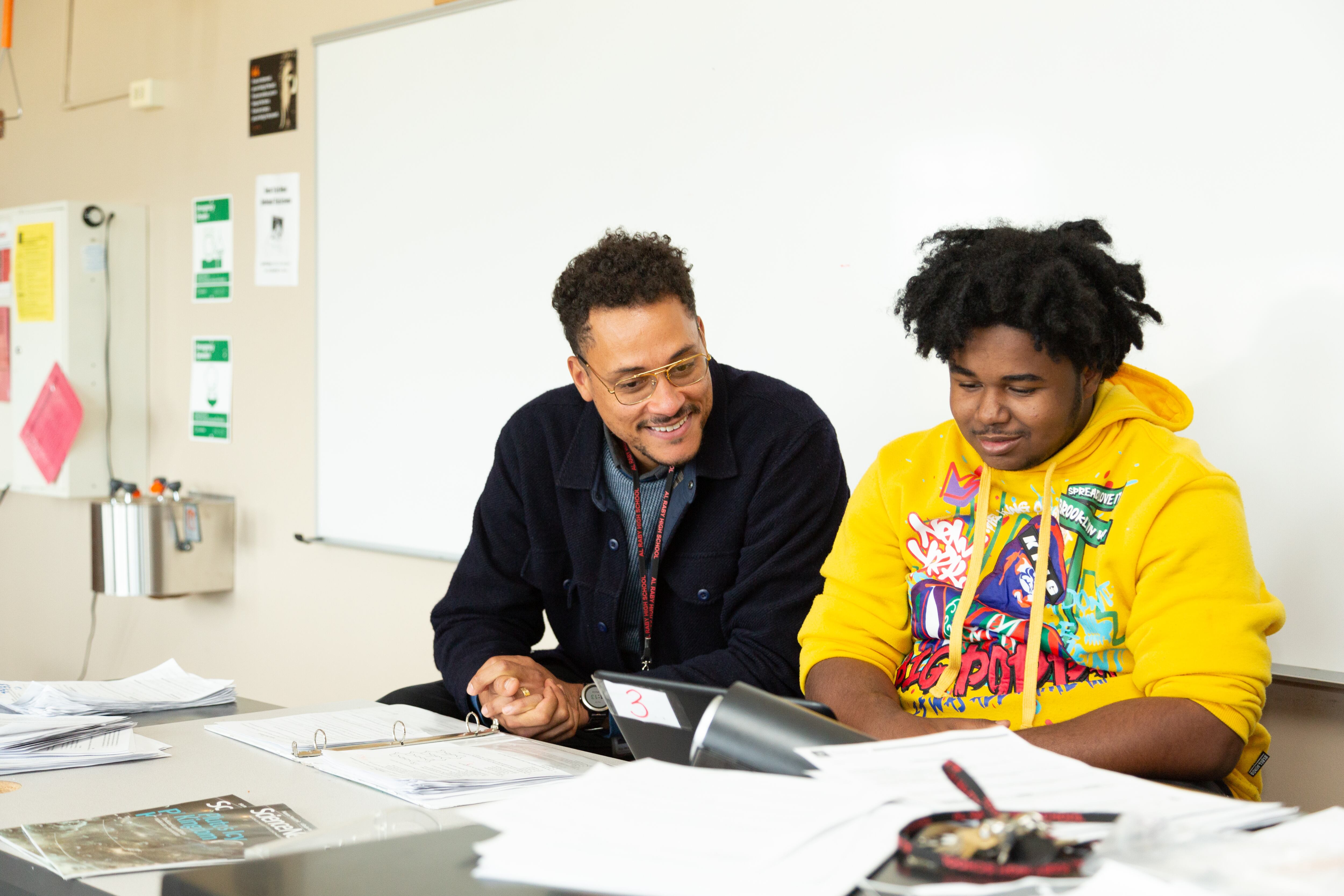 Nathaniel Joseph (on the left) sits with a student to work on an assignment. They are both sitting at a desk in a classroom.