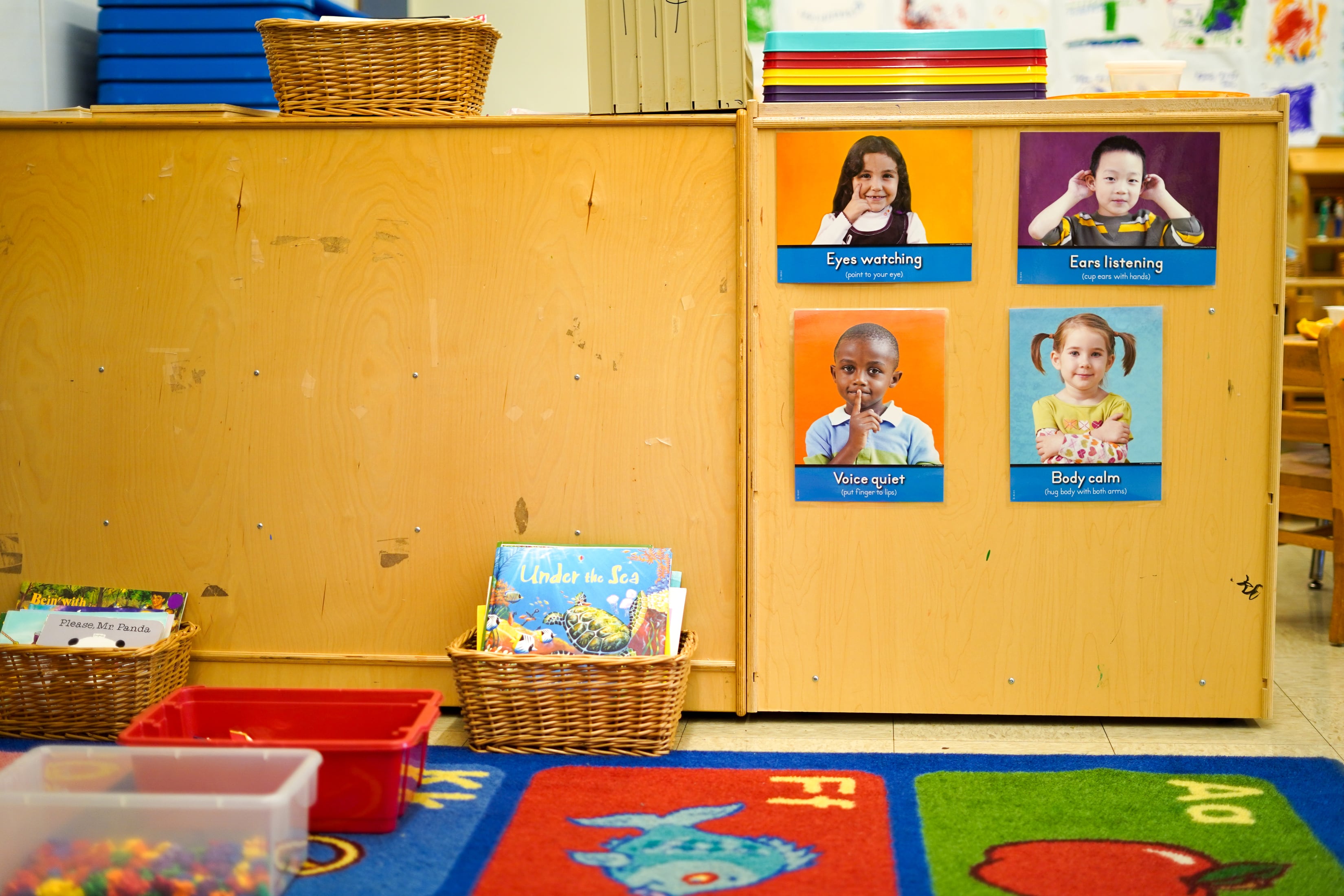 A shelf with four photos of children and a colorful classroom carpet. 