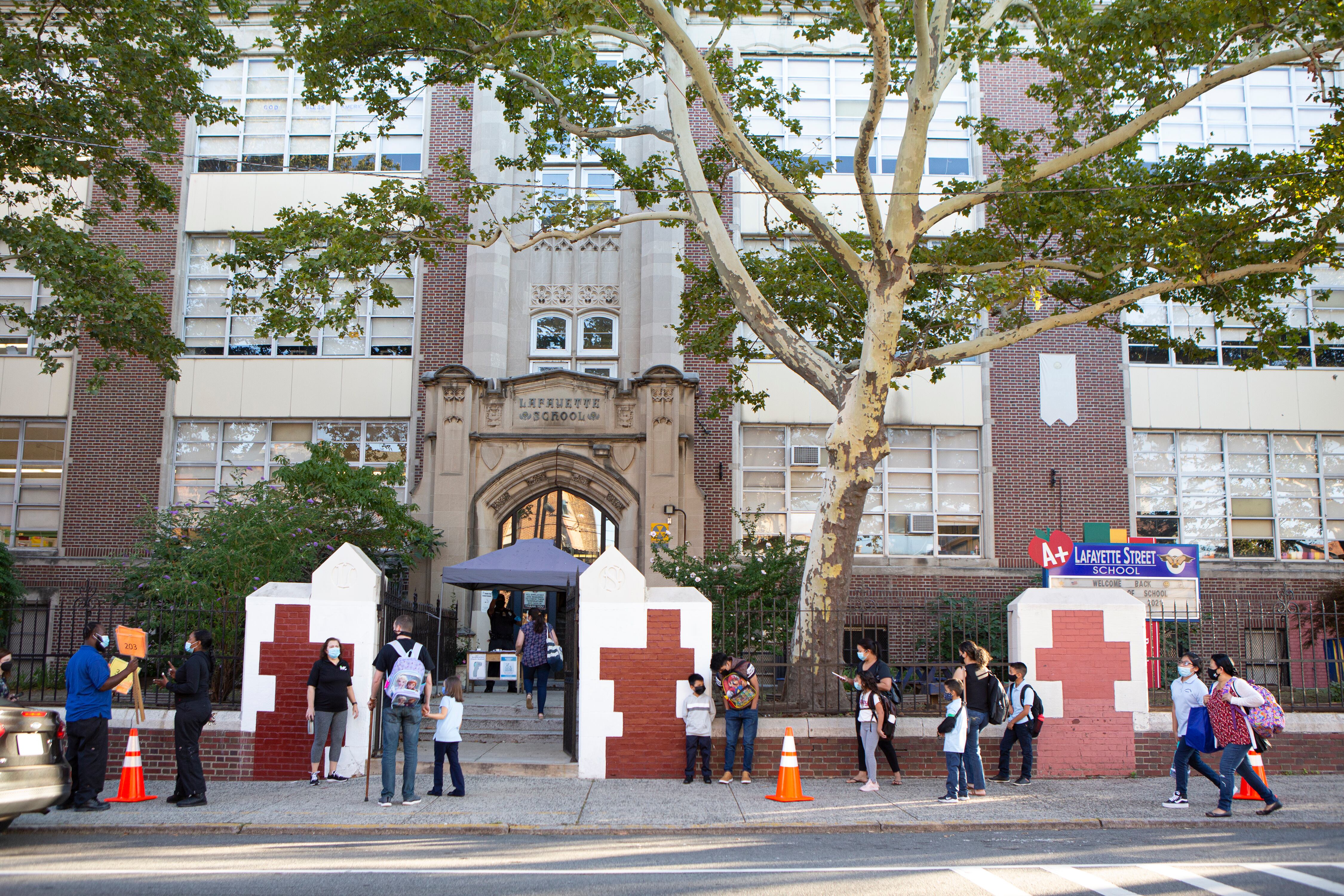 Students and parents stand outside Lafayette Street School, a big brick building with trees outside.