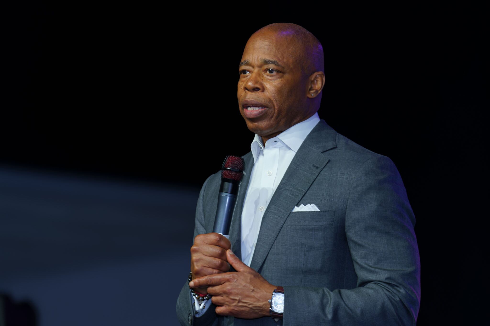 a man wearing a dark suit stands holding a microphone.