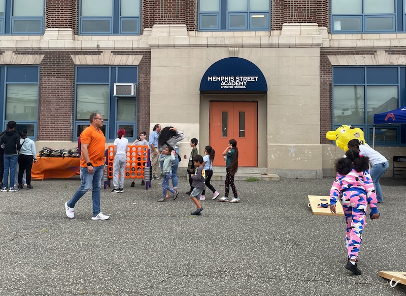 A photograph of a small group of children and a couple of adults outside the front entrance of a large school building.