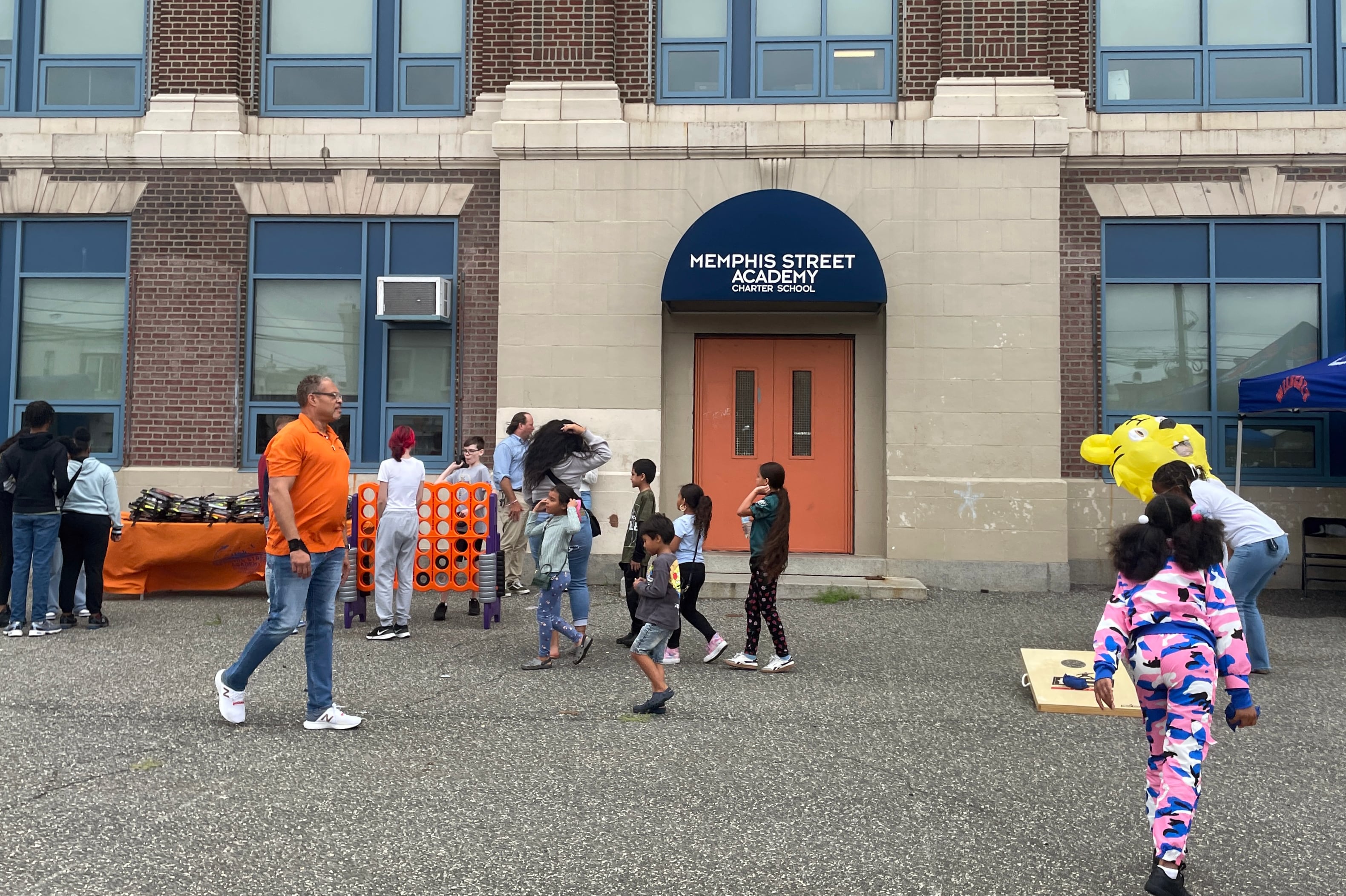 A photograph of a small group of children and a couple of adults outside the front entrance of a large school building.