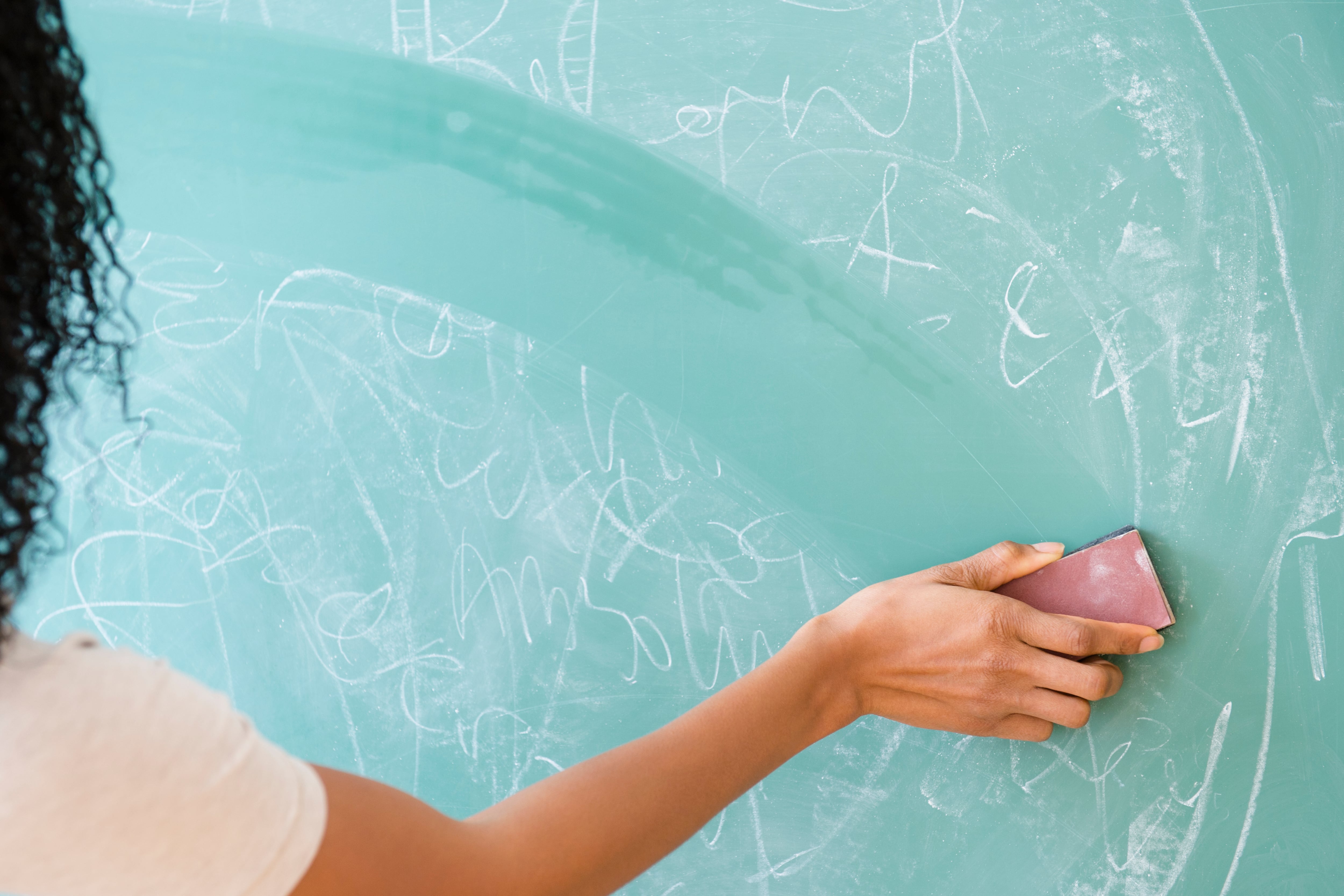 A woman uses her hand to erase something on a chalkboard.