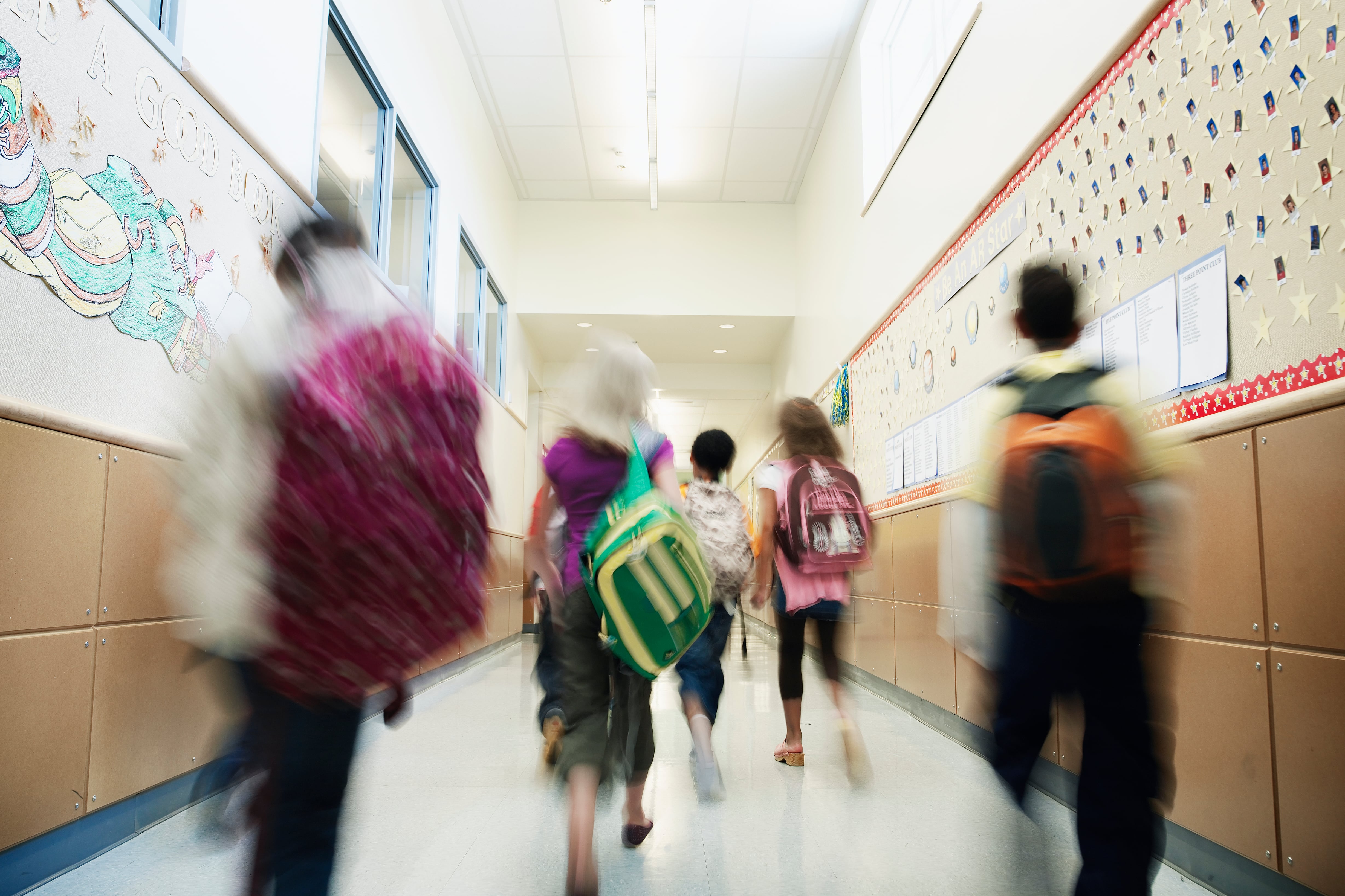 Young students with backpacks walking down hallway of elementary school.
