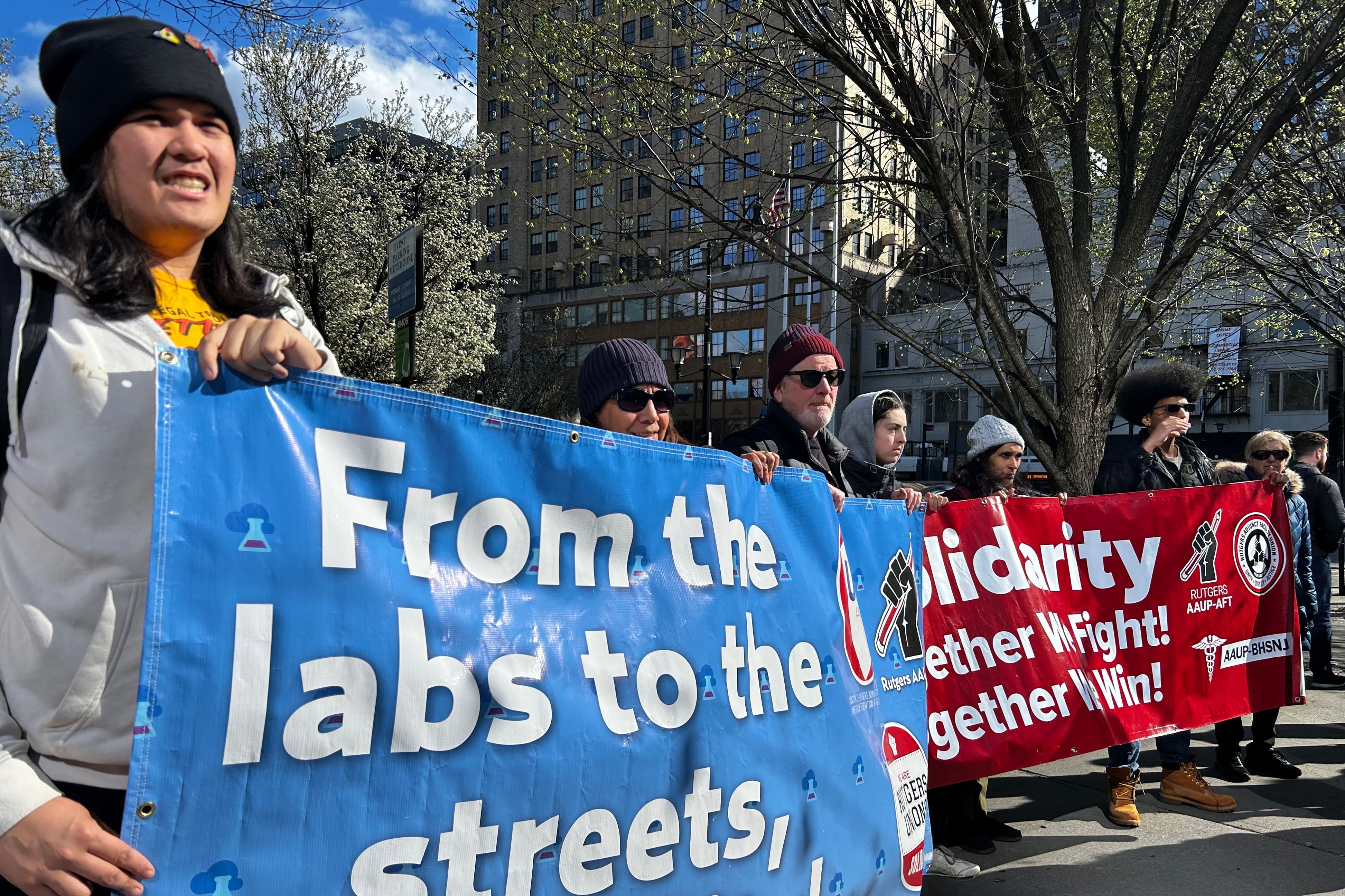 A group of adult hold signs during a rally outside.