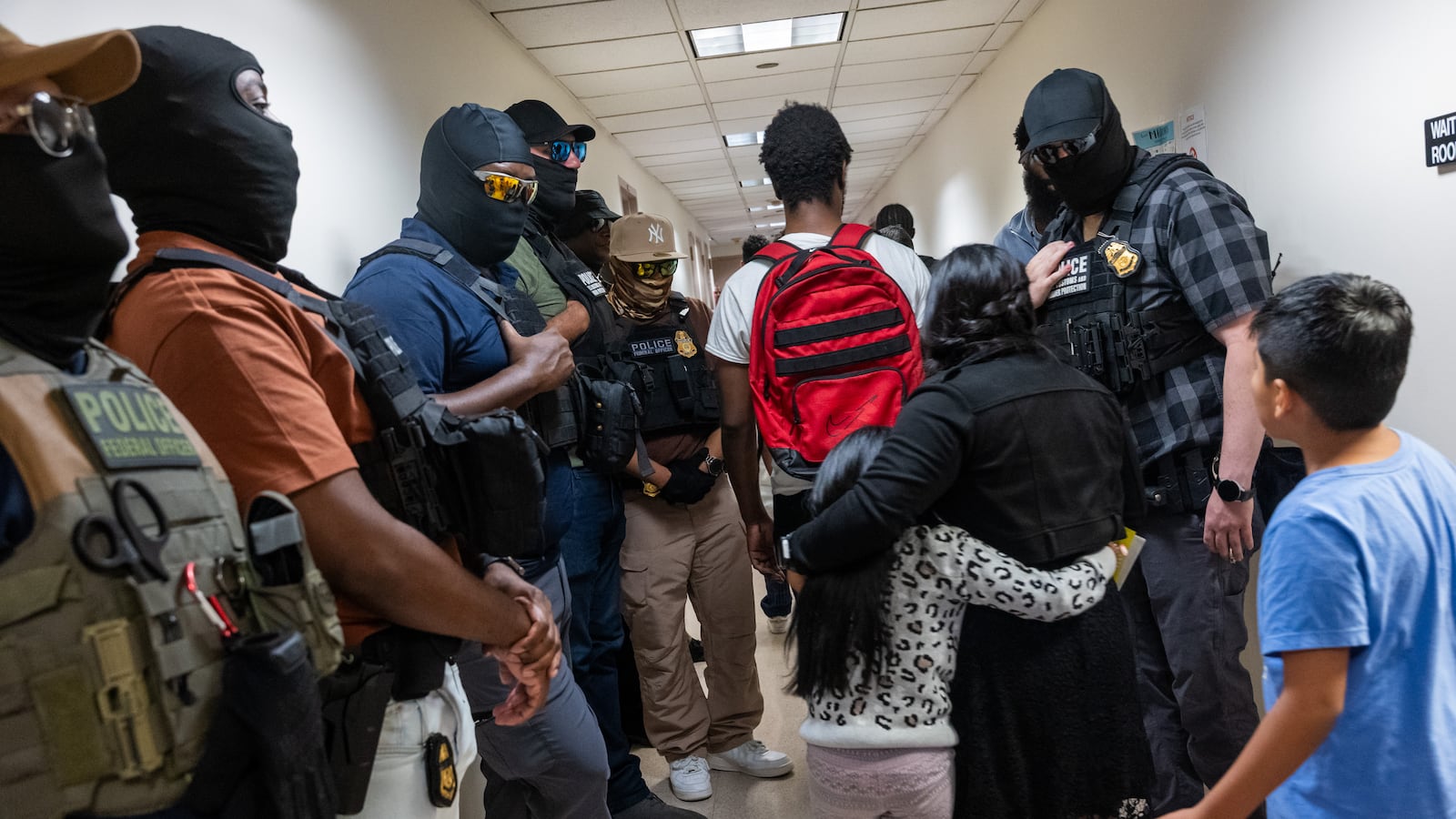 Federal agents, including members of ICE, patrol the halls of immigration court, as a family walks by.