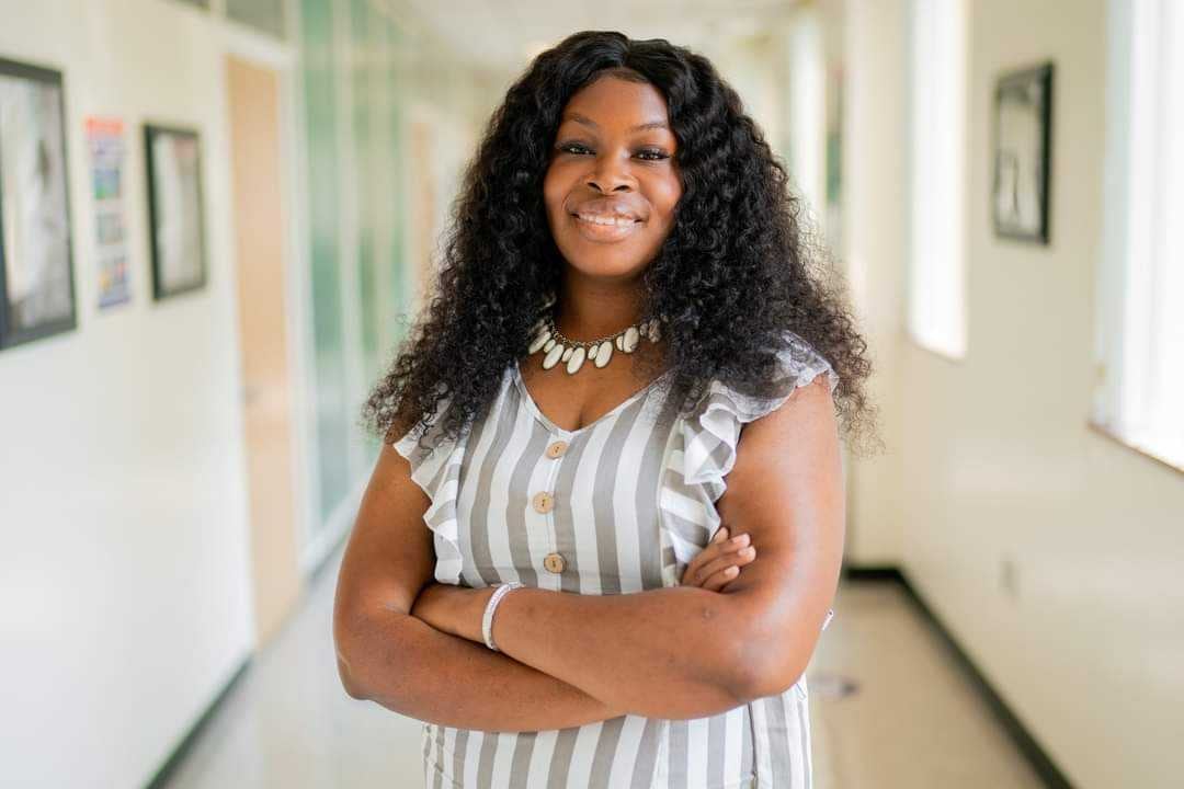 Woman poses for a photo, crossing her arms in a school hallway