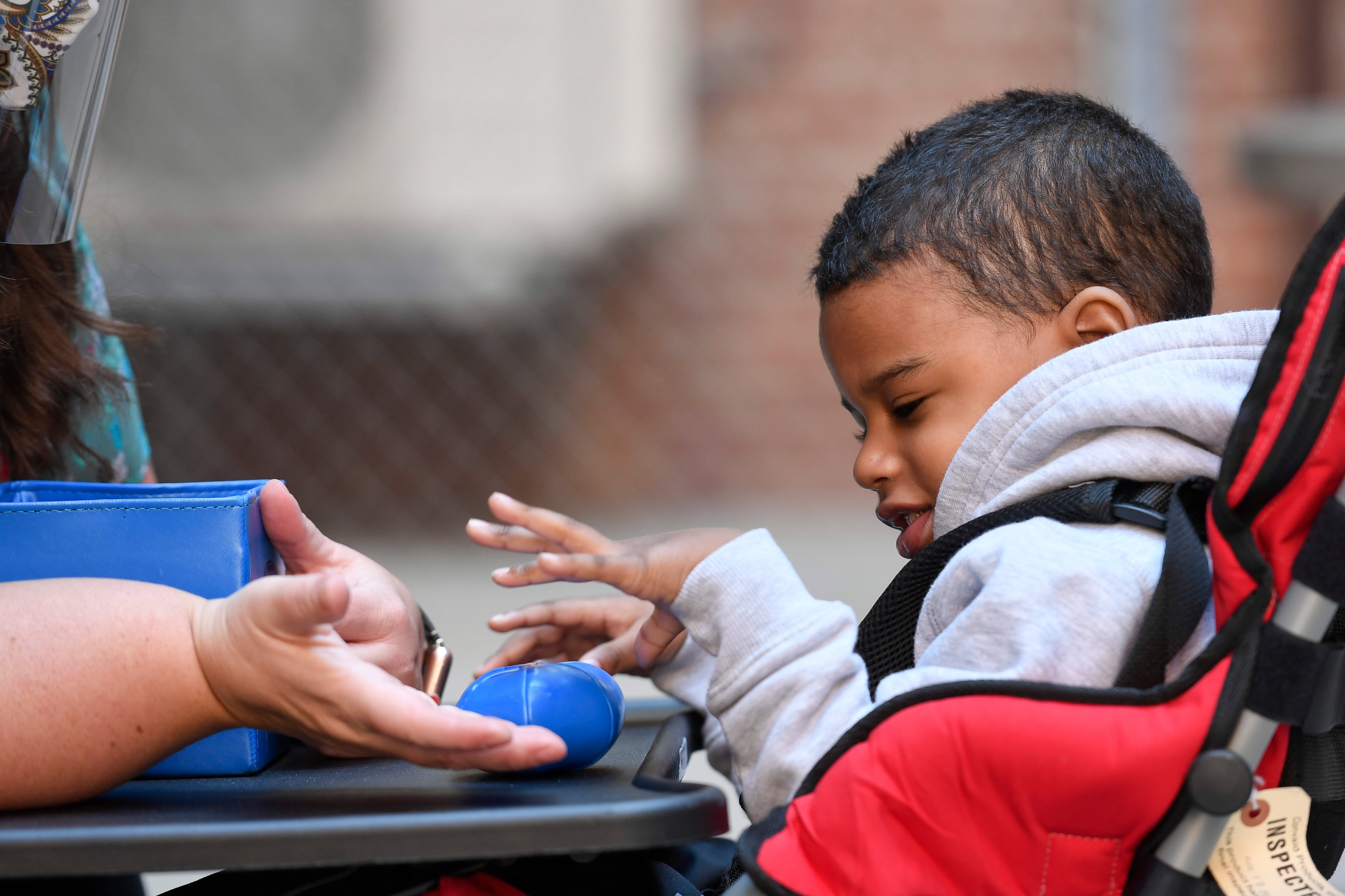 A little boy in a sweatshirt touches things while working with a teacher.