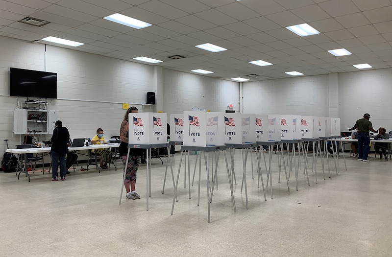 Two rows of voting booths line the middle of a bright, tile-floor room