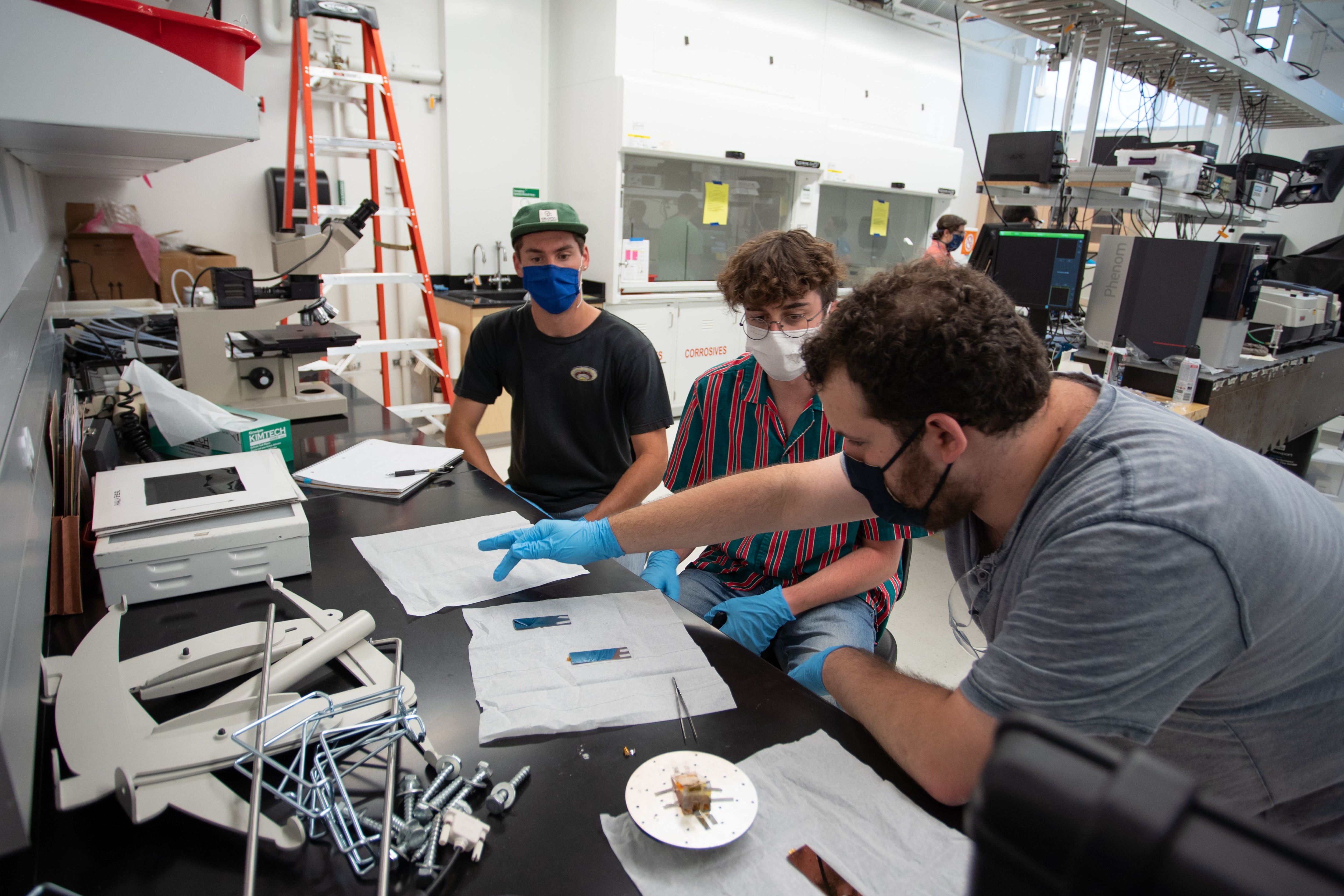 Three students wearing blue gloves gather around a work table in a lab class at the Colorado School of Mines. One student points at a paper.