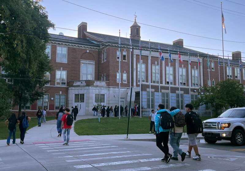 A photograph of students crossing the street in front of a large stone school building.