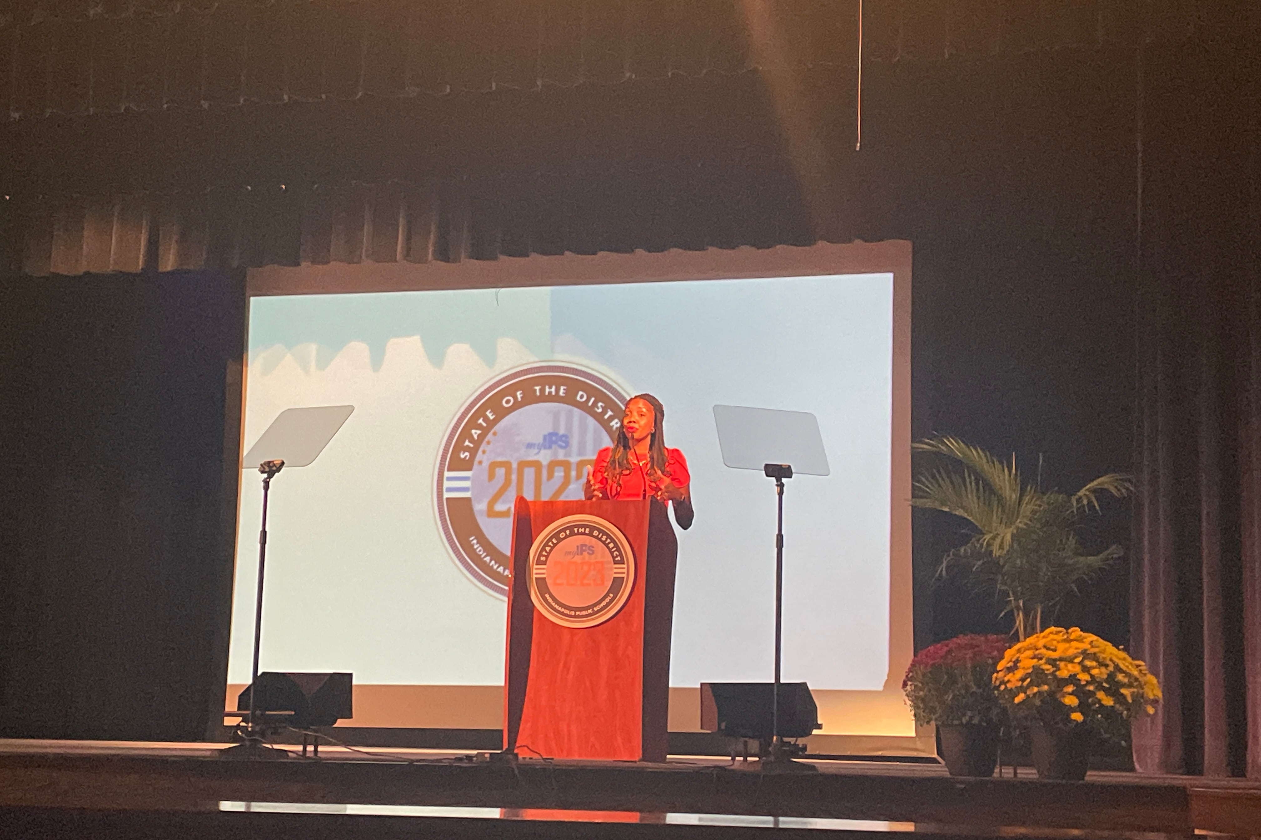 A woman stands on stage behind a podium.
