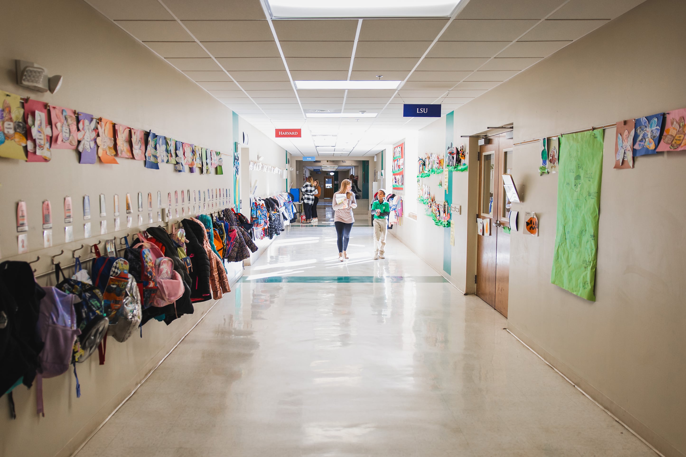 An adult and a child walk down a colorful school hallway.