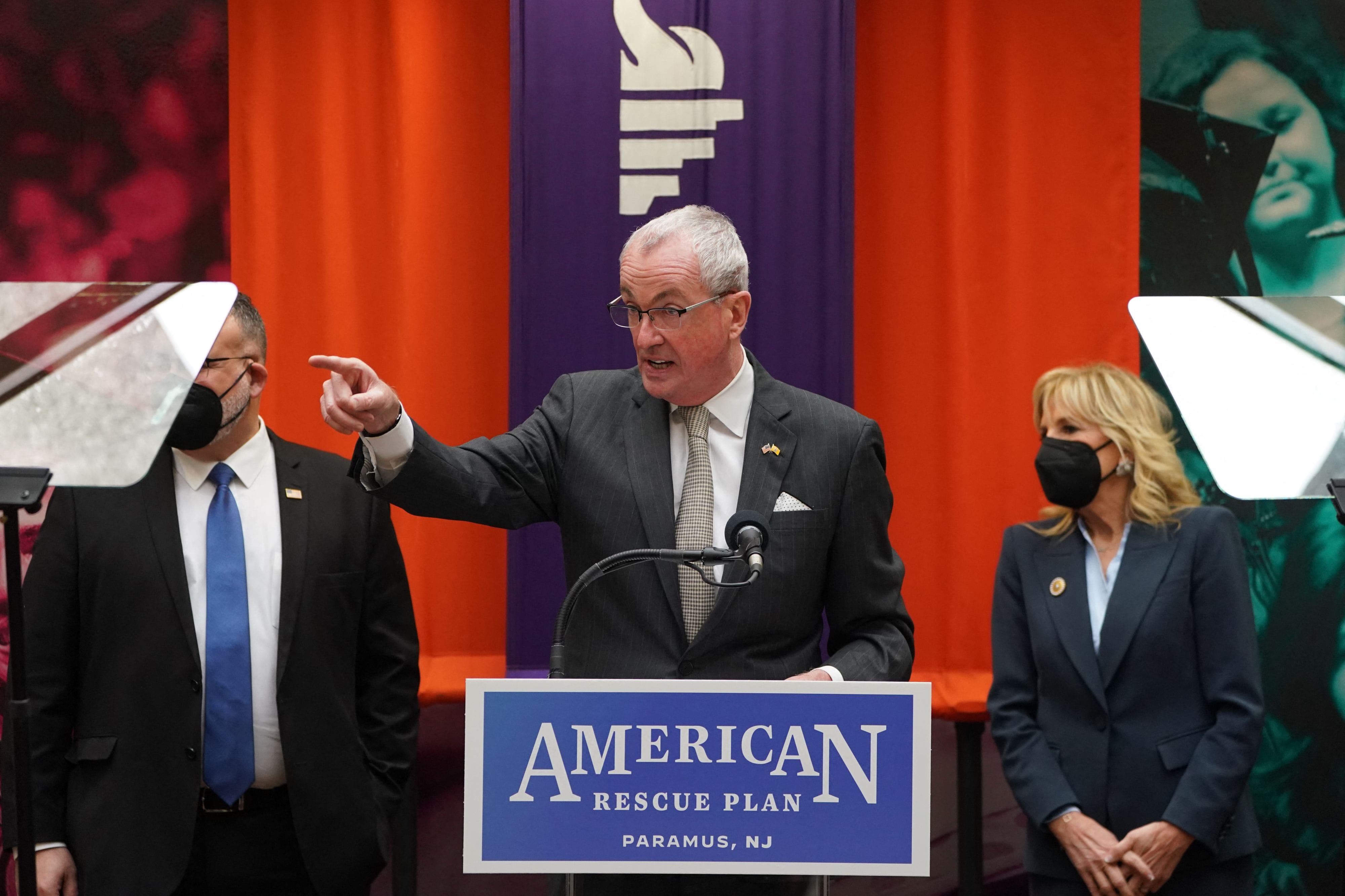New Jersey Governor Phil Murphy points his finger and speaks to conference attendees. U.S. Secretary of Education Miguel Cardona and first lady Dr. Jill Biden stand behind him.