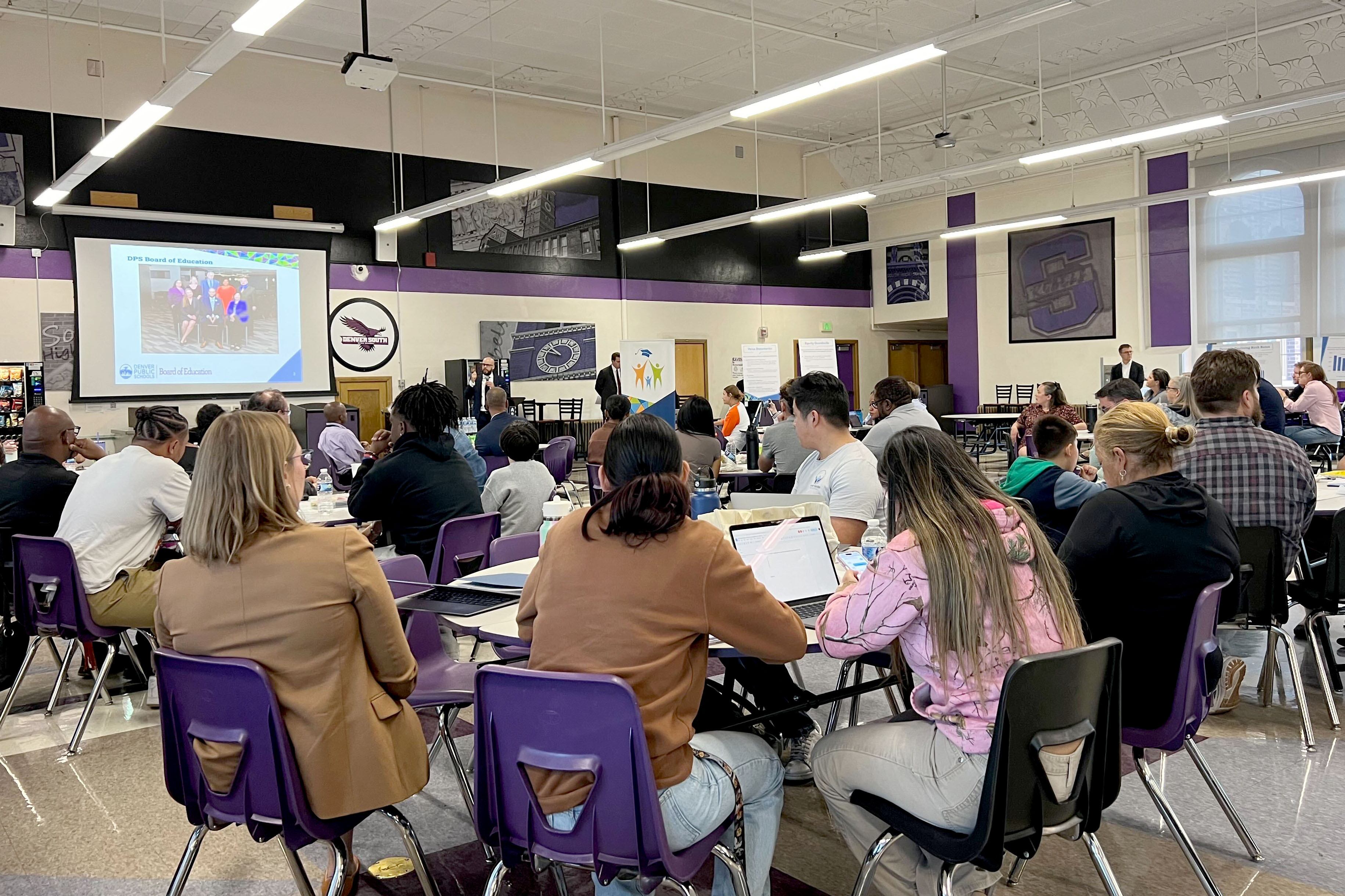 A room full of people sitting in chairs in a large school room.