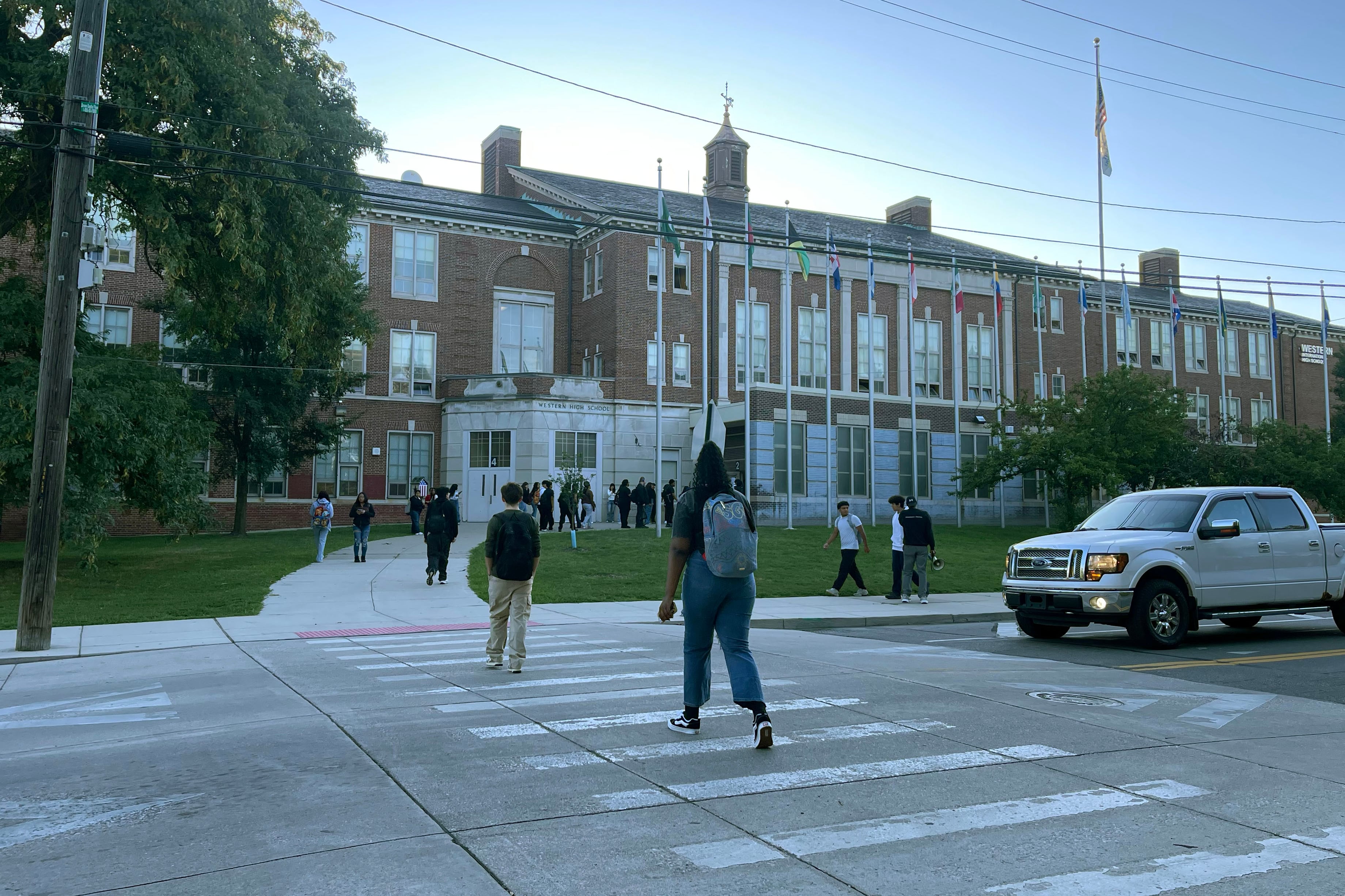 A photograph of students crossing the street in front of a large stone school building.
