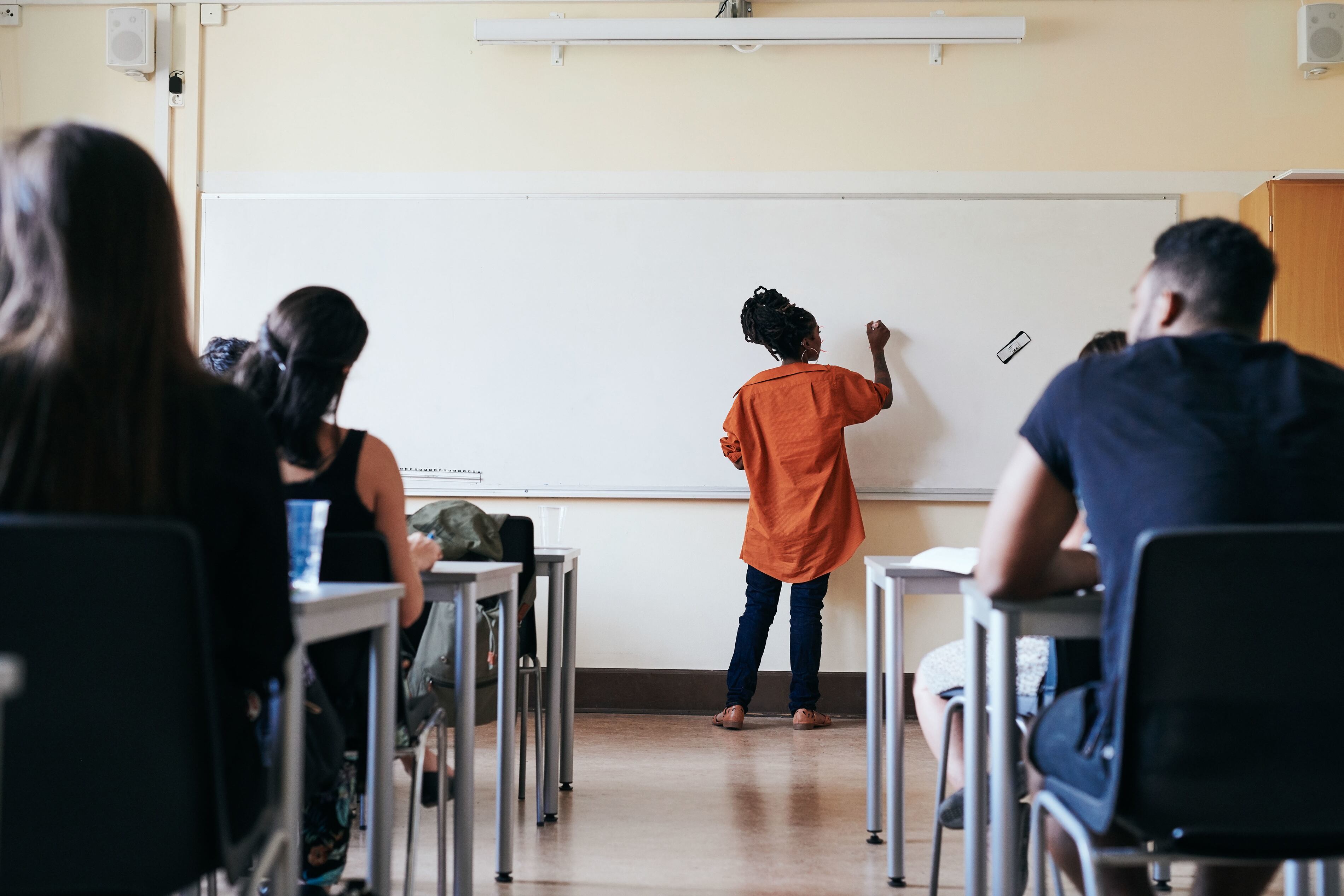 Students watch as their teacher writes on the whiteboard in a classroom.