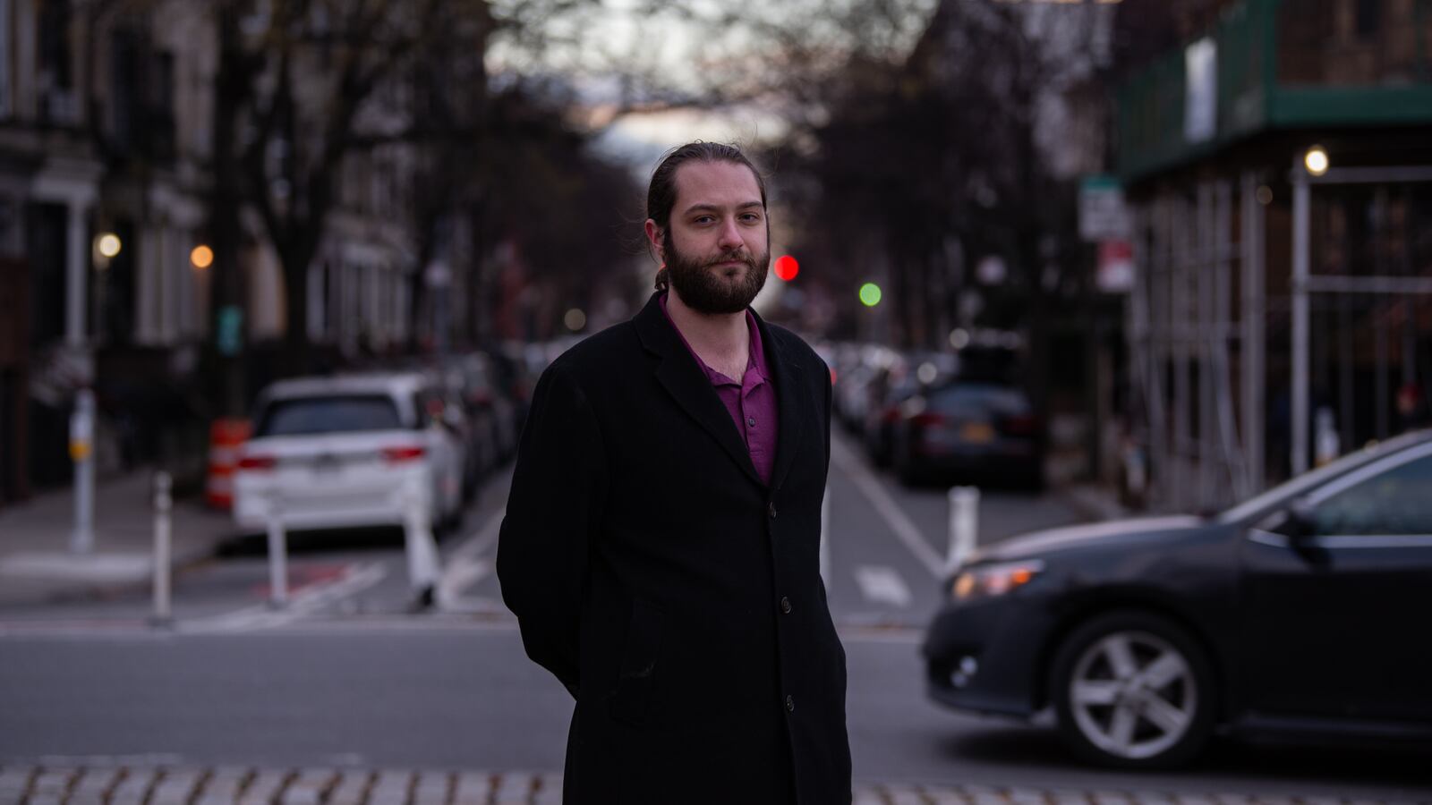 A man in a black coat stands in a city street.