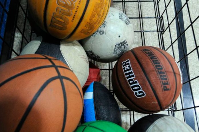 Basketballs, soccer balls, and a blue football sit in a shopping cart.