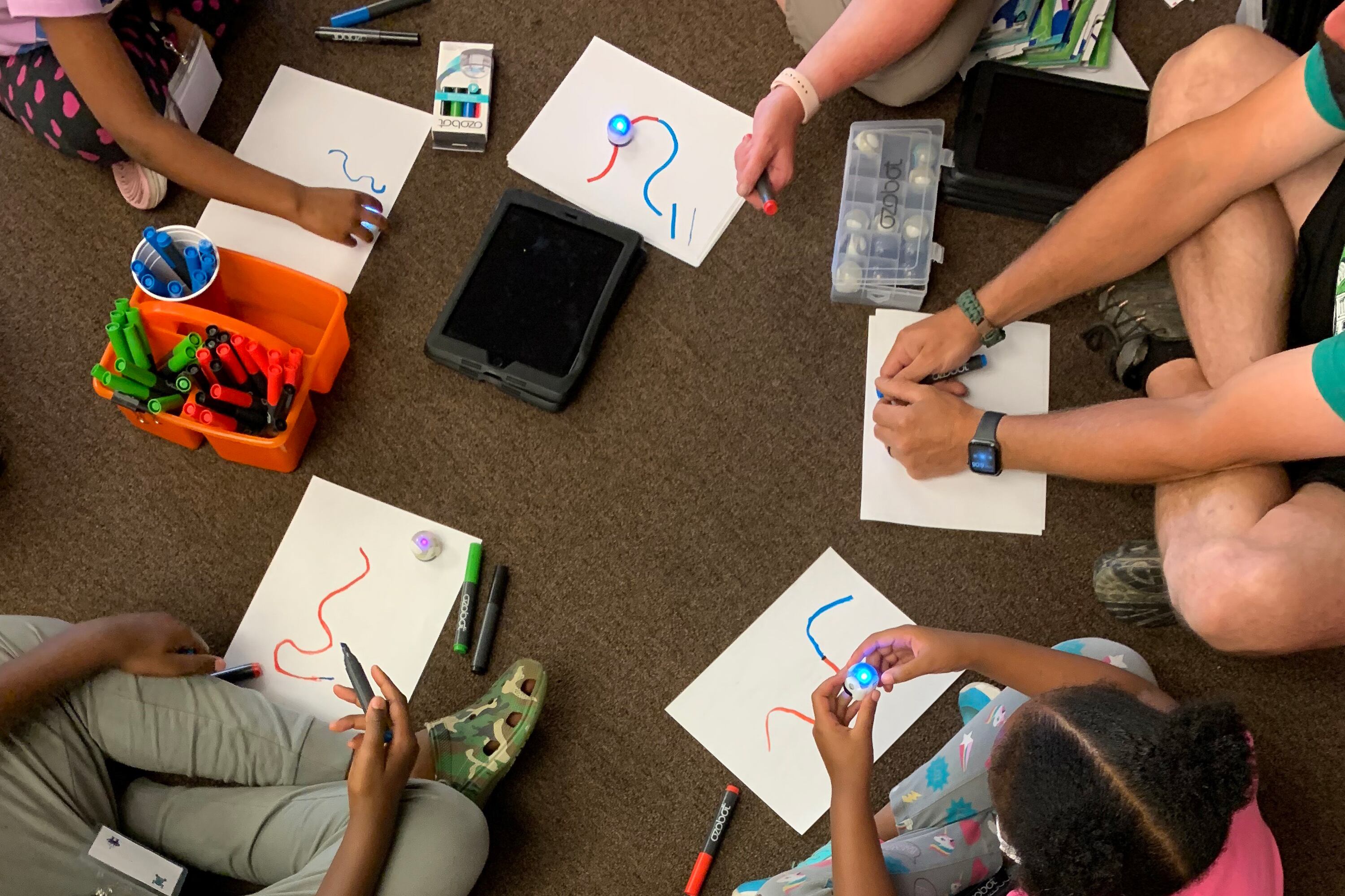 Overhead shot looking down at a tutor and three students sitting on the floor drawing.