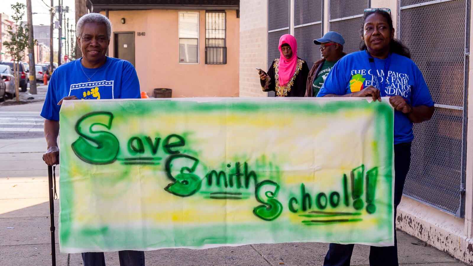 Two people holding a green and yellow banner that reads: Save smith schools.