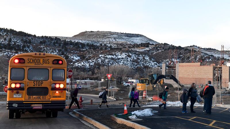 A yellow school bus drops off students with a mountain in the background.