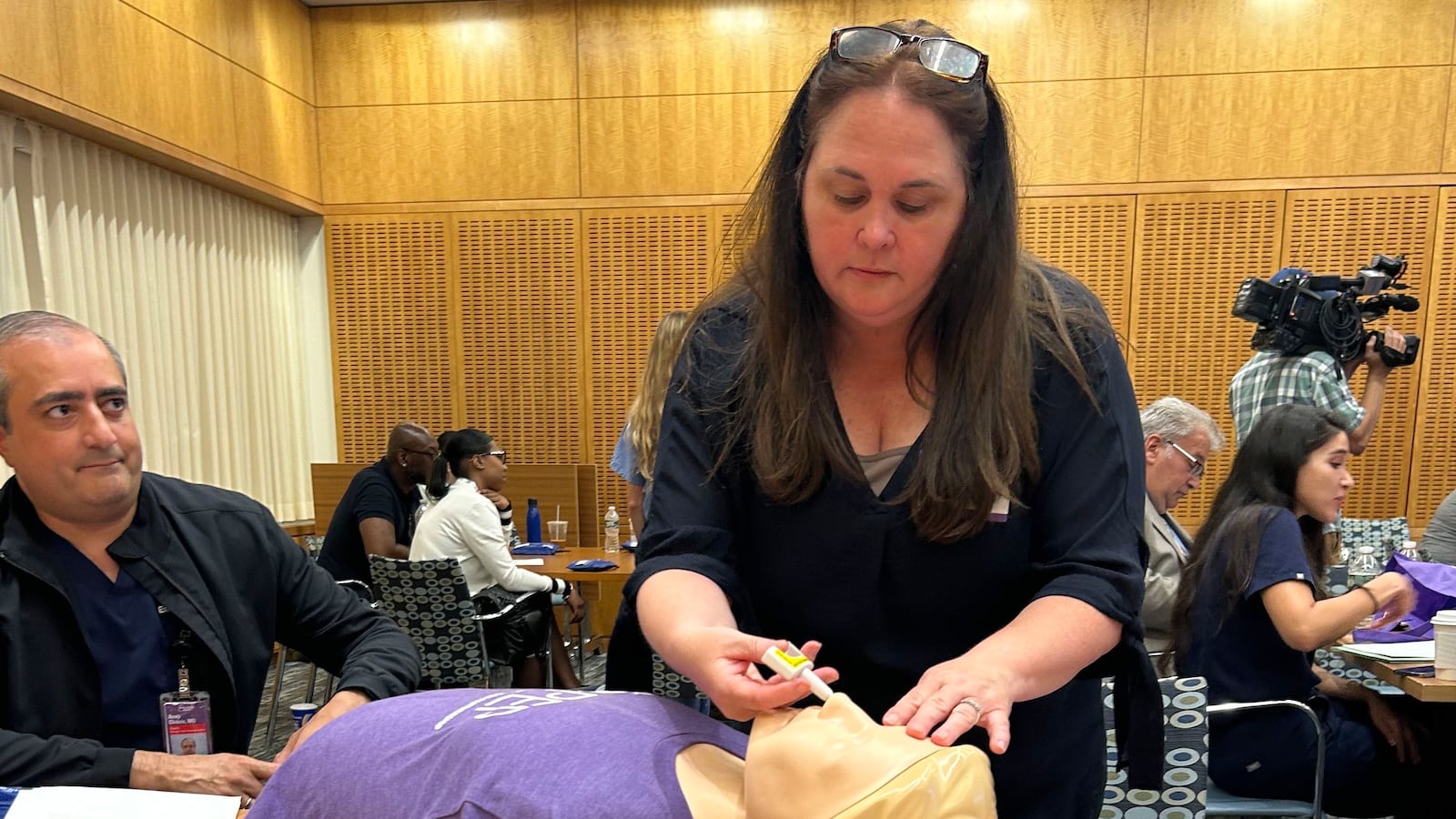 A woman with long dark hair practices giving narcan to a practice doll.