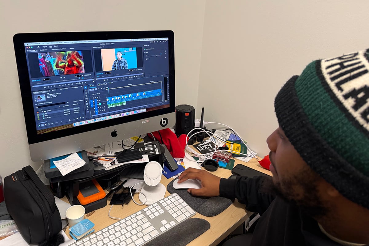 A man in a greet hat works in front of a computer.