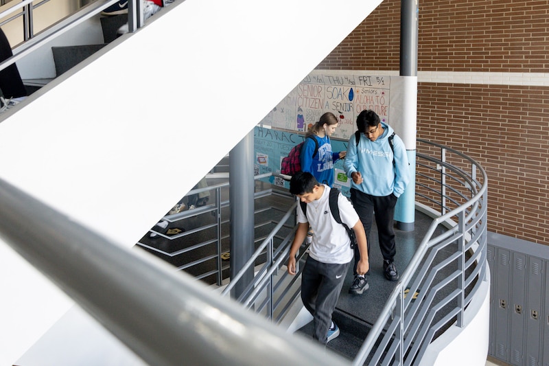 Three high school students walking along a stairway inside of a school building.