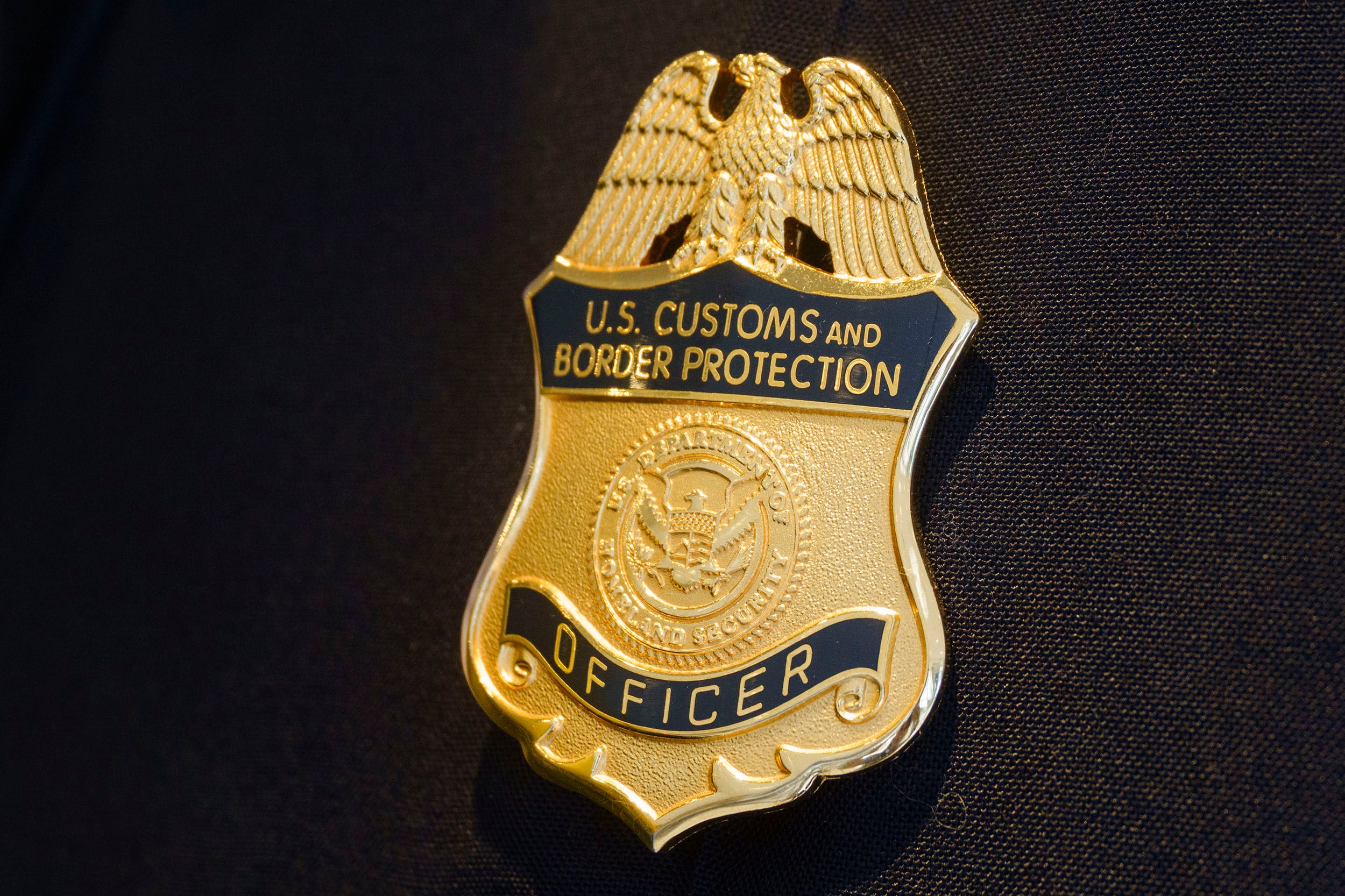 An up-close photograph of a gold colored badge that reads "U.S. Customs and Border Protection Officer."